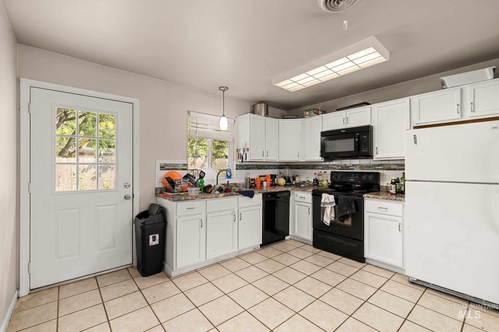 Kitchen with black appliances, backsplash, white cabinetry, decorative light fixtures, and light tile patterned floors