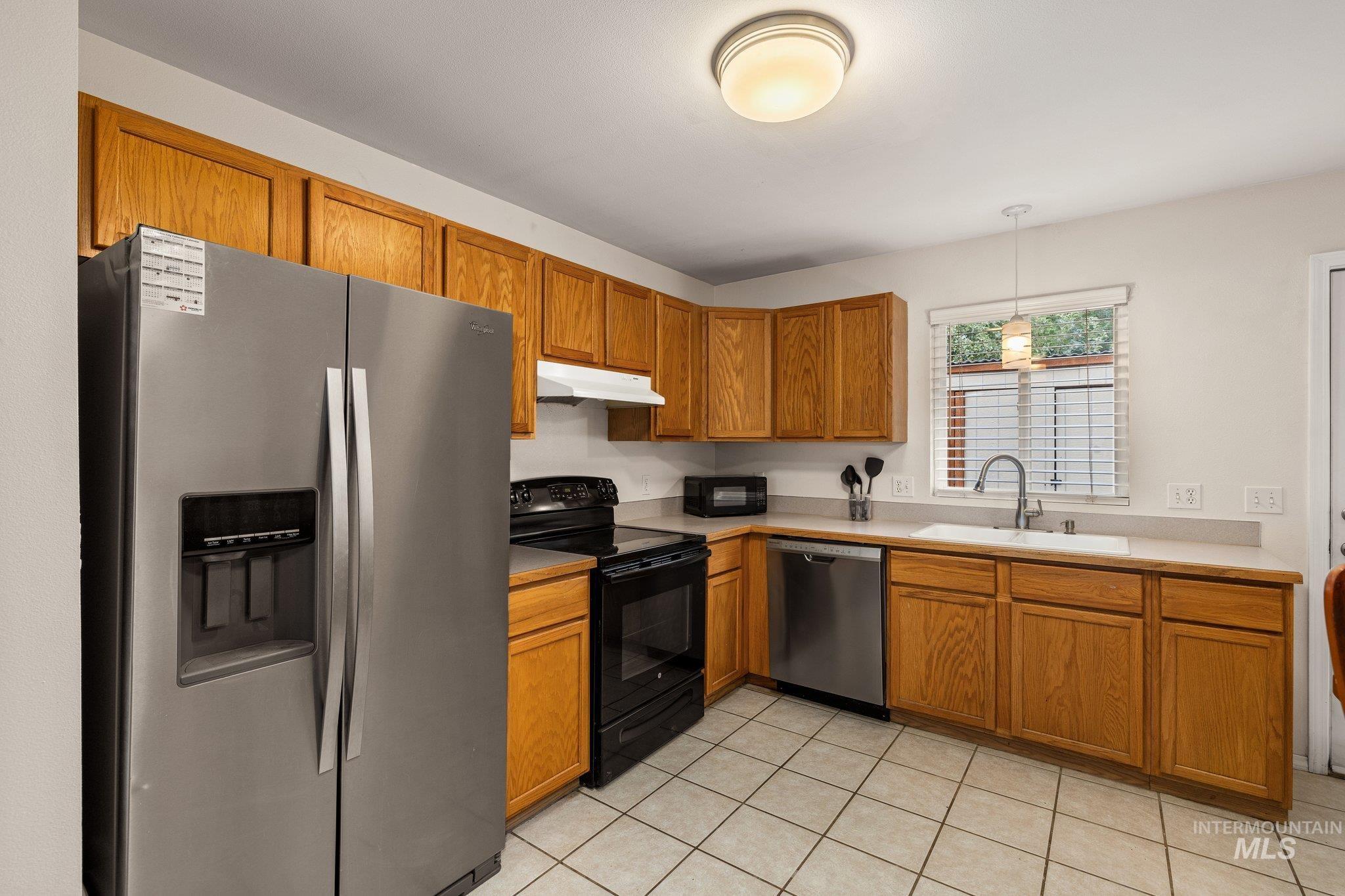 Kitchen with black appliances, pendant lighting, brown cabinetry, and light countertops