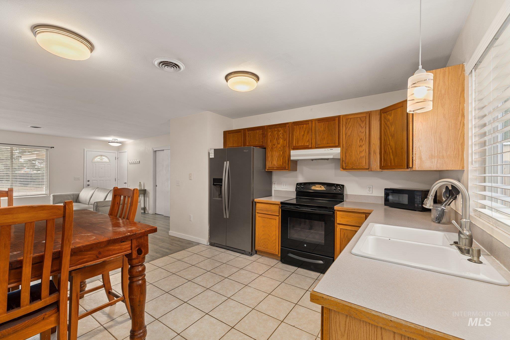 Kitchen featuring light countertops, black appliances, decorative light fixtures, light tile patterned floors, and brown cabinets