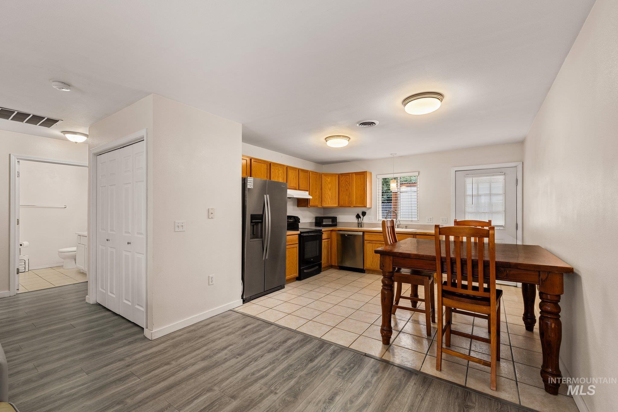 Kitchen with brown cabinetry, appliances with stainless steel finishes, light countertops, light wood-style flooring, and under cabinet range hood