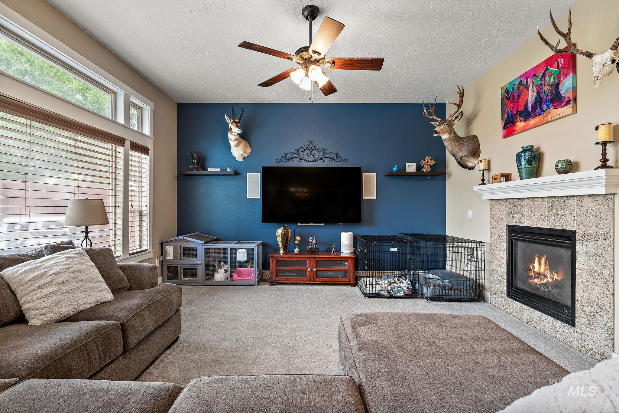 Living area featuring a tiled fireplace, carpet flooring, ceiling fan, and a textured ceiling