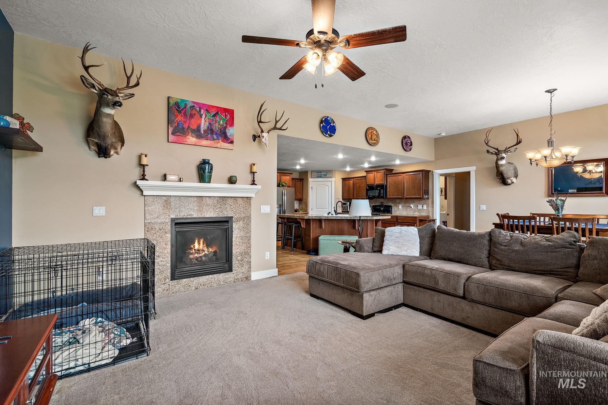 Living room featuring a fireplace, a chandelier, ceiling fan, light colored carpet, and a textured ceiling