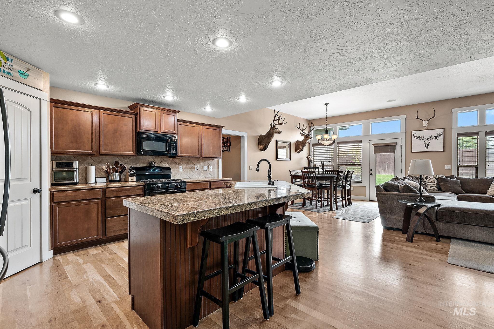 Kitchen with a breakfast bar, an island with sink, a textured ceiling, decorative backsplash, and black appliances