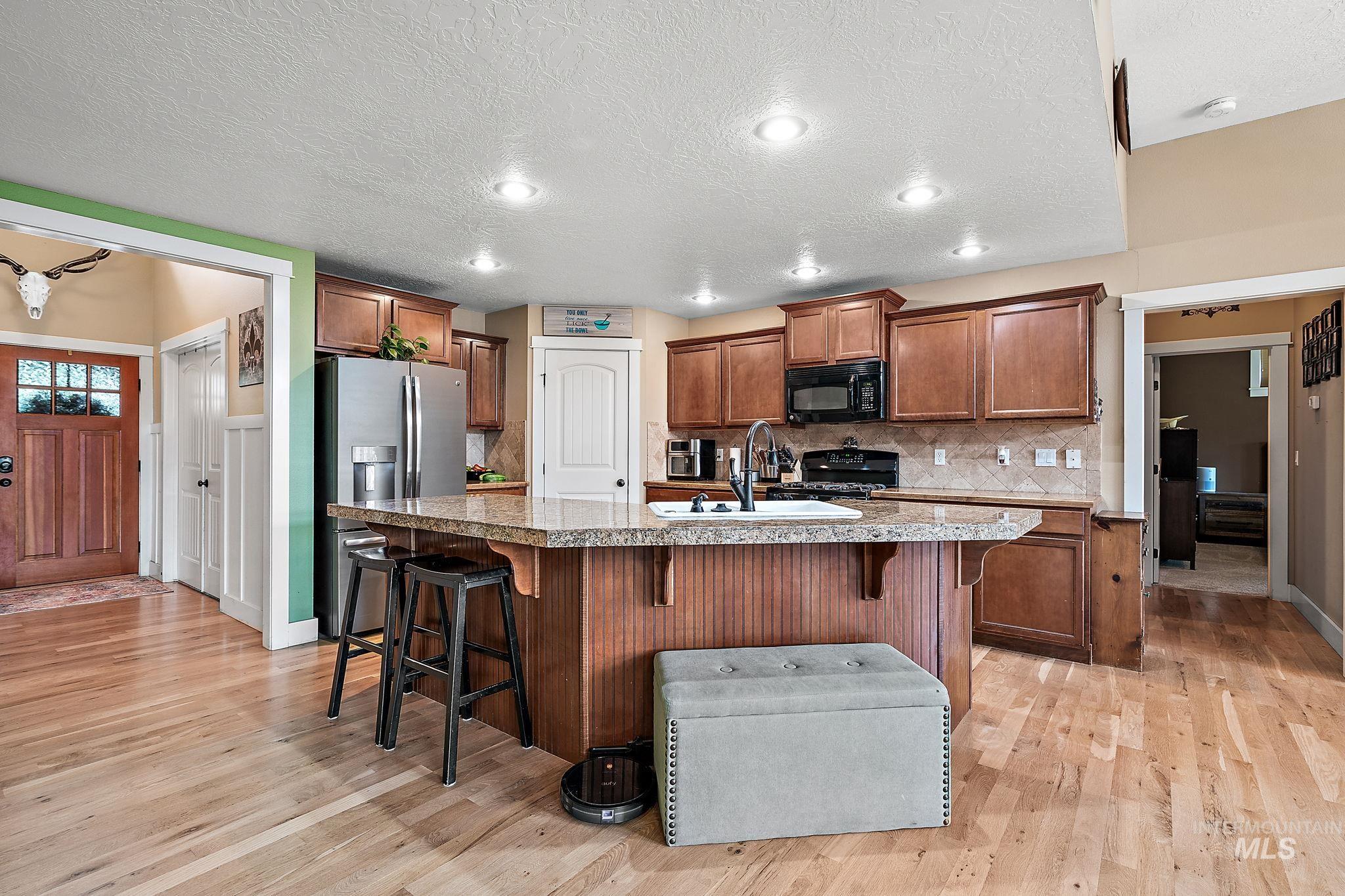 Kitchen with a breakfast bar area, brown cabinets, a textured ceiling, an island with sink, and tasteful backsplash
