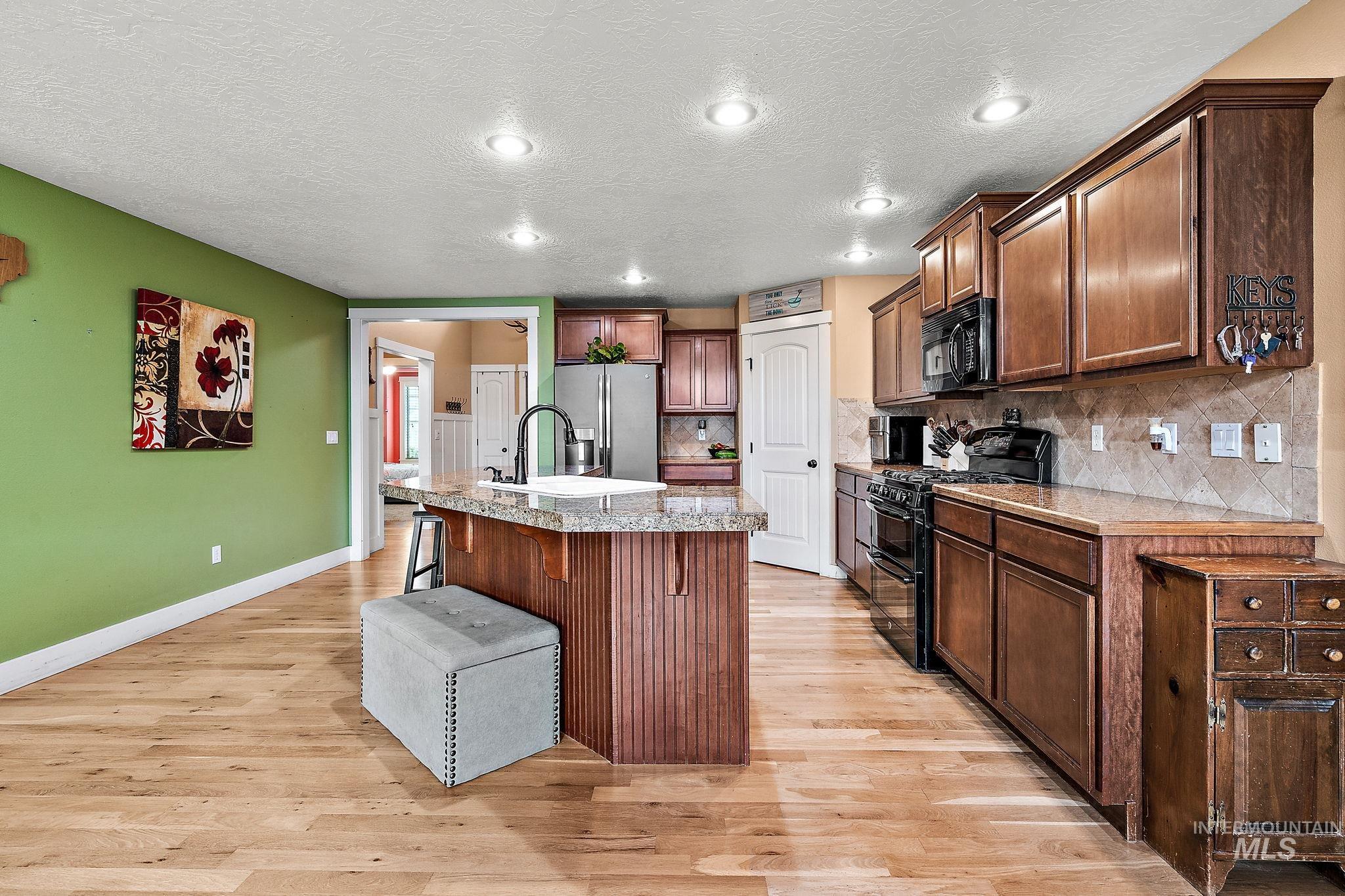 Kitchen with a kitchen bar, black appliances, a kitchen island with sink, a textured ceiling, and light wood-type flooring