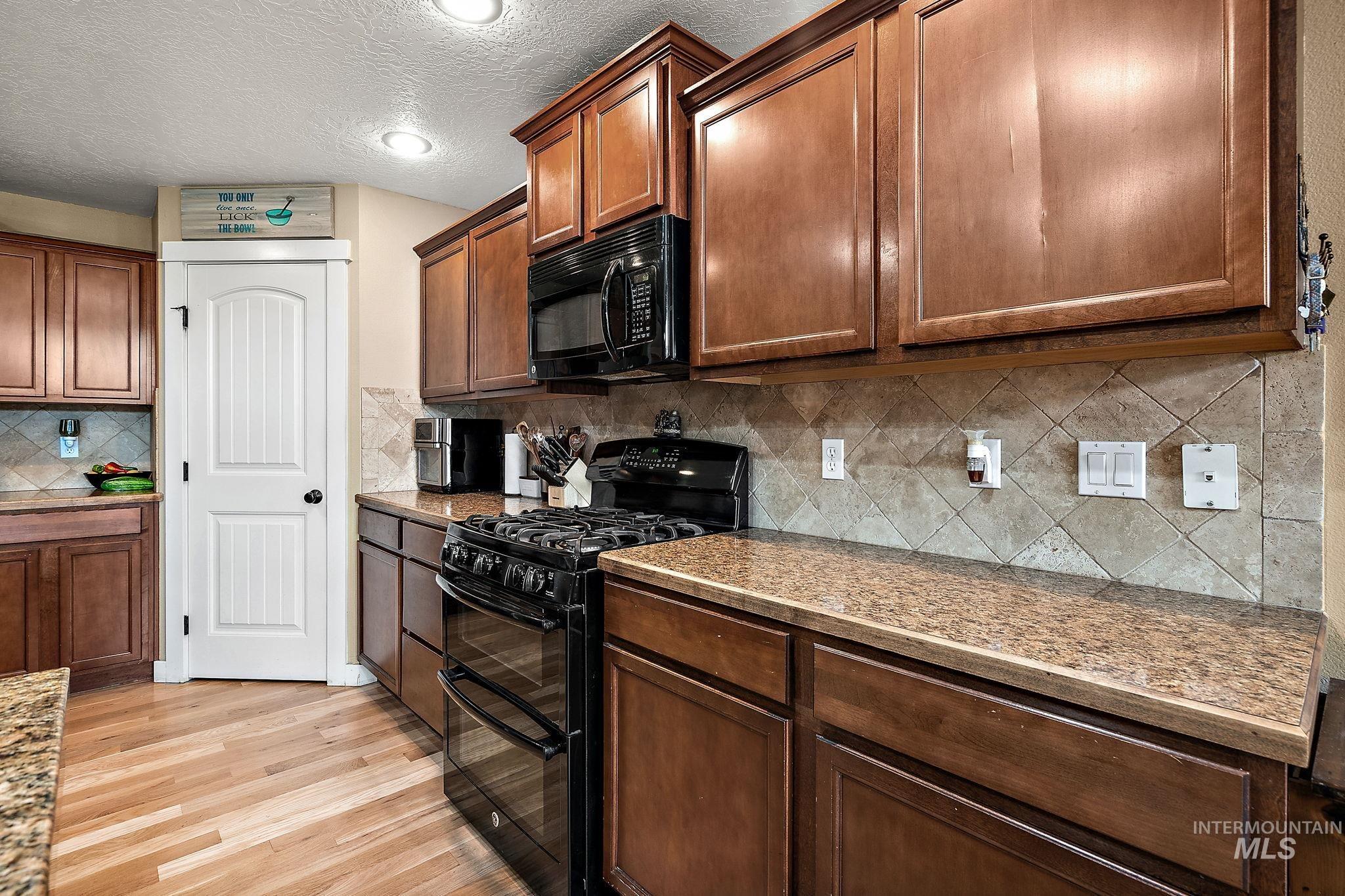 Kitchen featuring black appliances, a textured ceiling, light wood finished floors, tasteful backsplash, and brown cabinetry