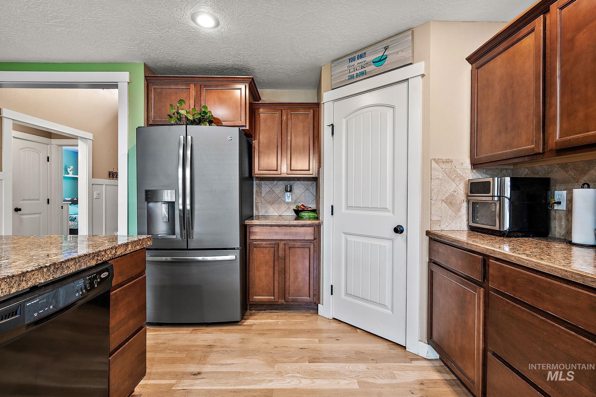 Kitchen featuring dishwasher, stainless steel fridge, a textured ceiling, light wood-style flooring, and tasteful backsplash