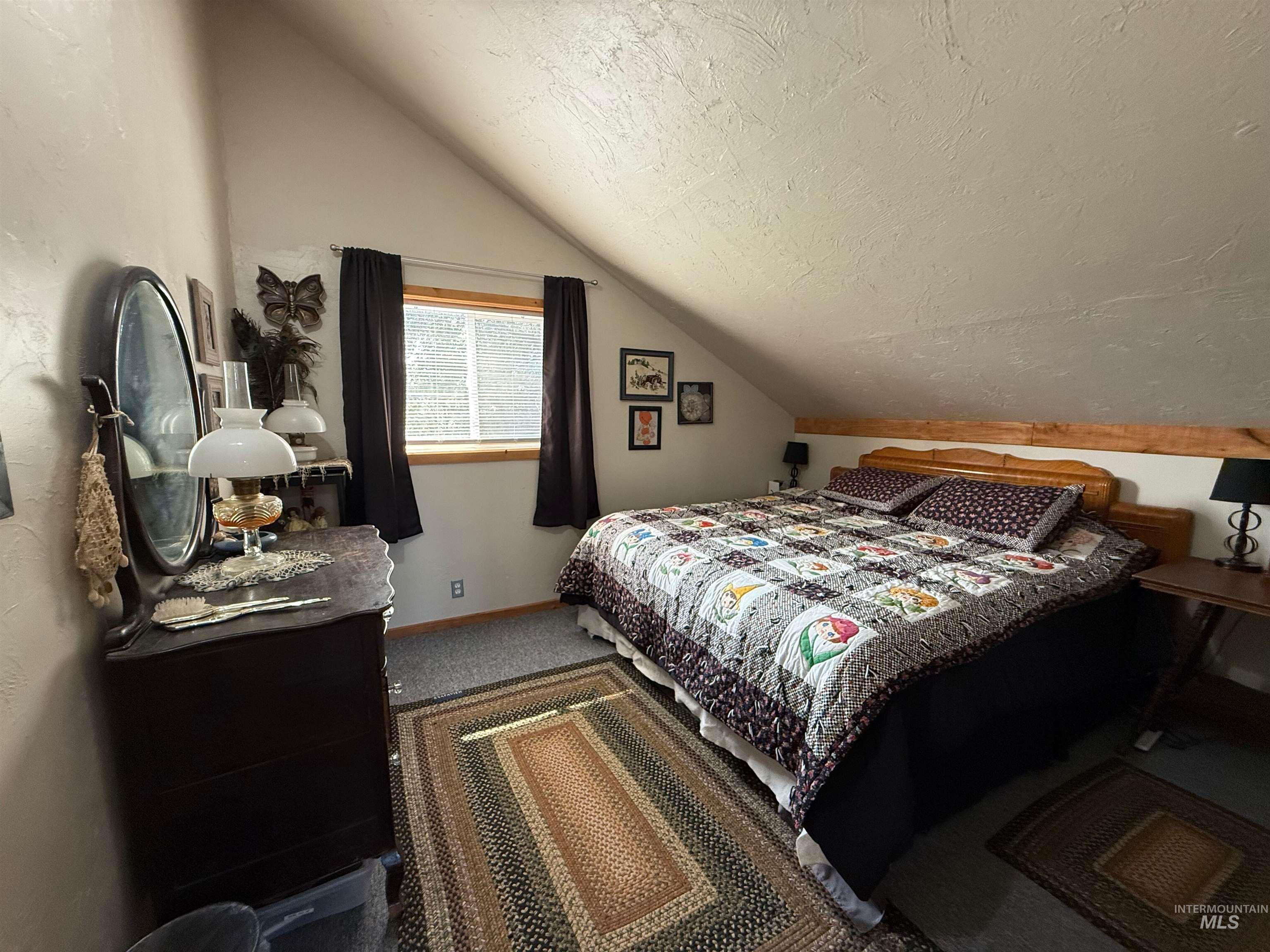 Bedroom with a textured ceiling, carpet floors, and lofted ceiling