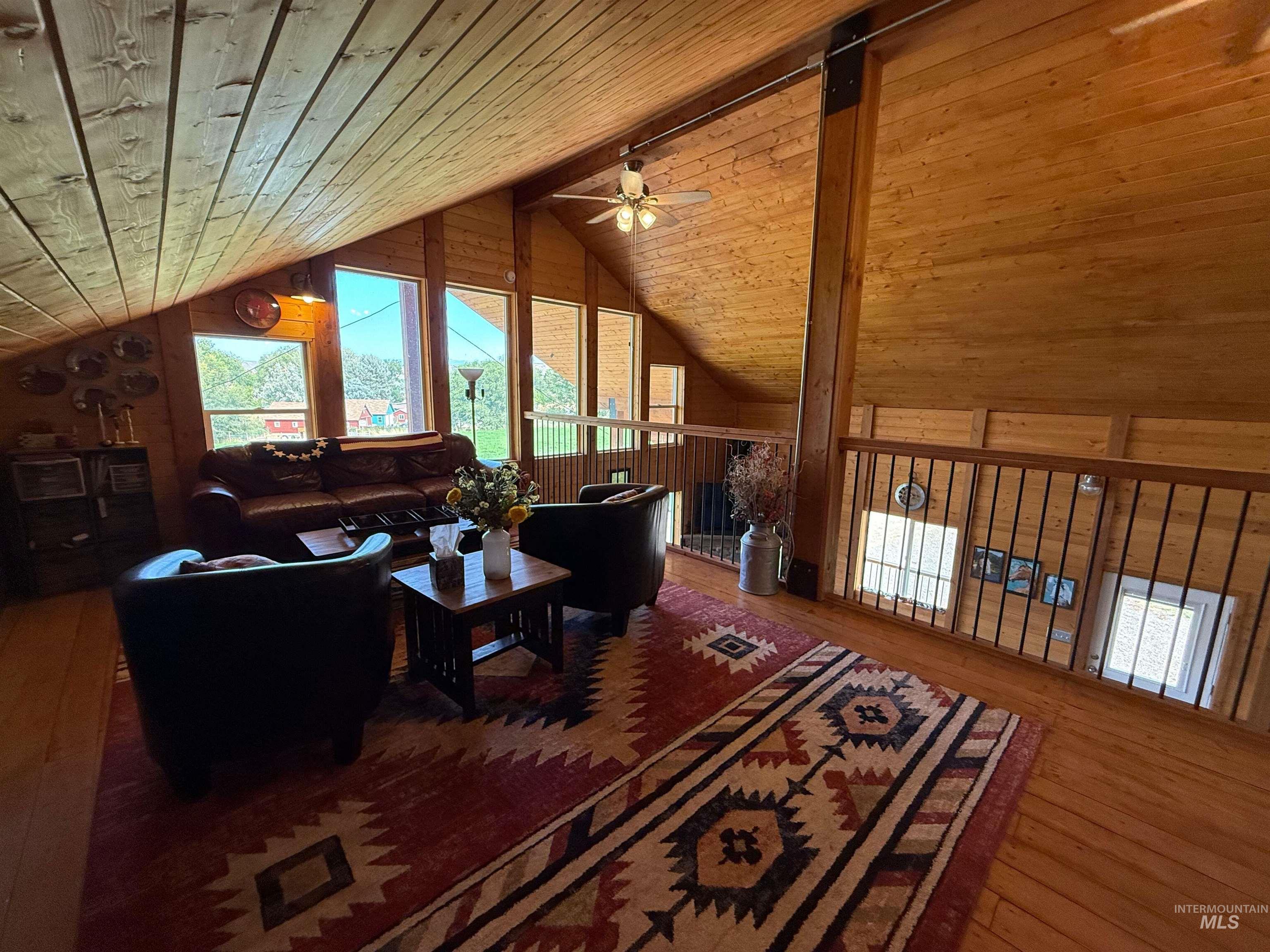 Living area with plenty of natural light, hardwood / wood-style floors, wooden ceiling, wood walls, and ceiling fan