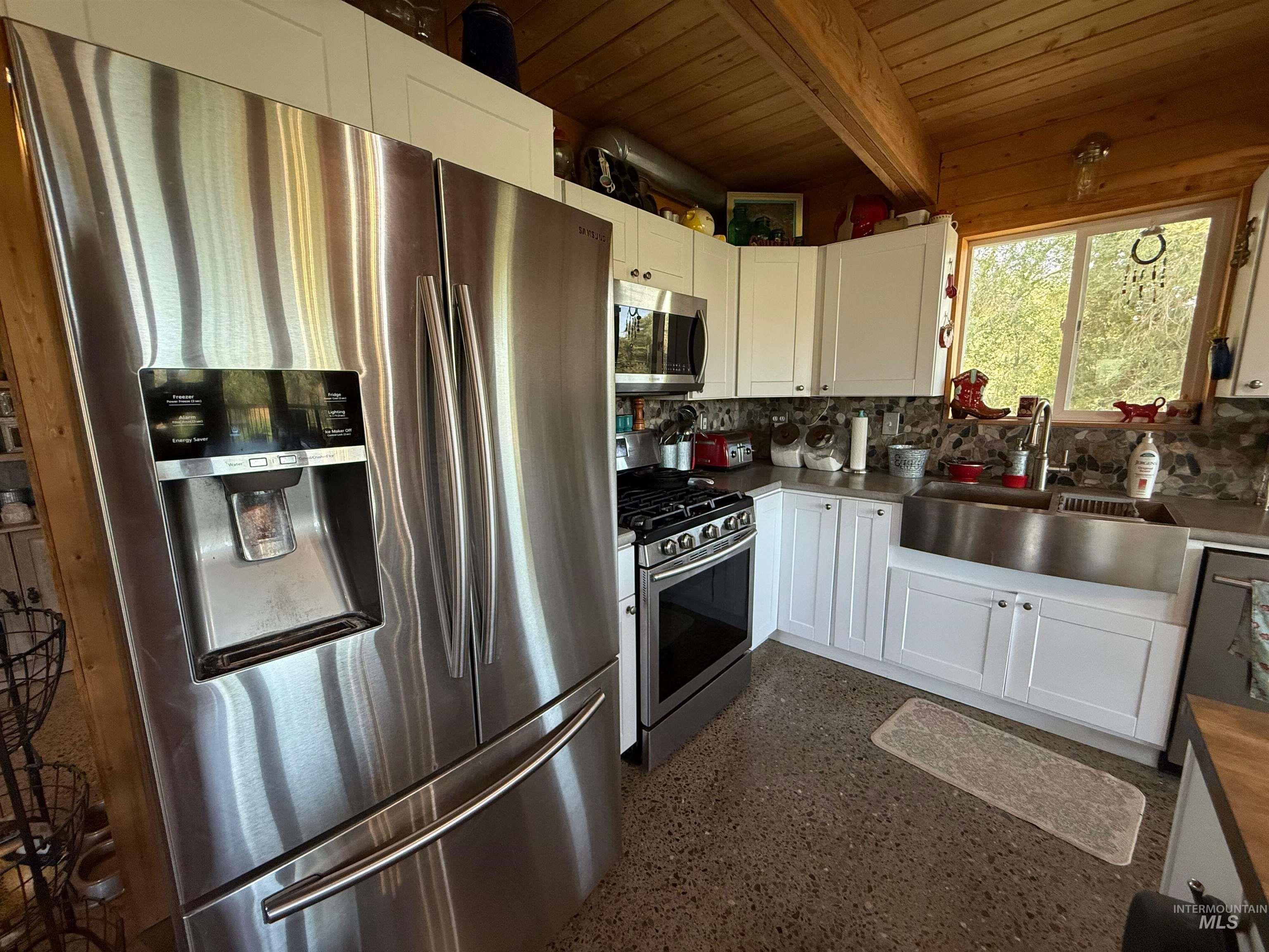 Kitchen with stainless steel appliances, white cabinetry, a wooden ceiling with exposed beams, light speckled floor, and backsplash