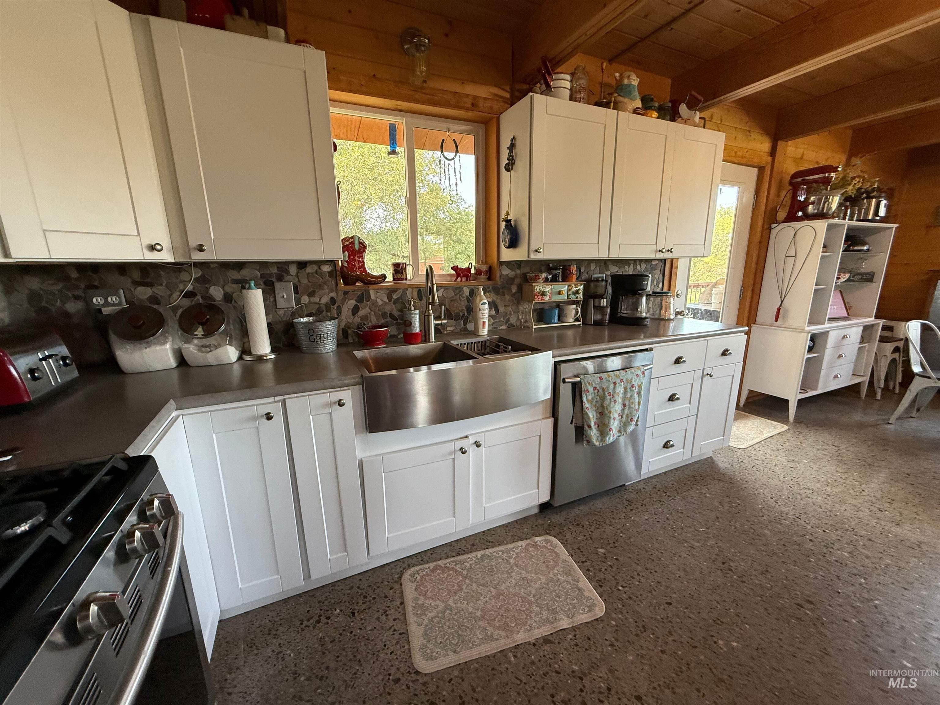 Kitchen with gas range, white cabinets, a wooden ceiling with exposed beams, stainless steel dishwasher, and dark countertops