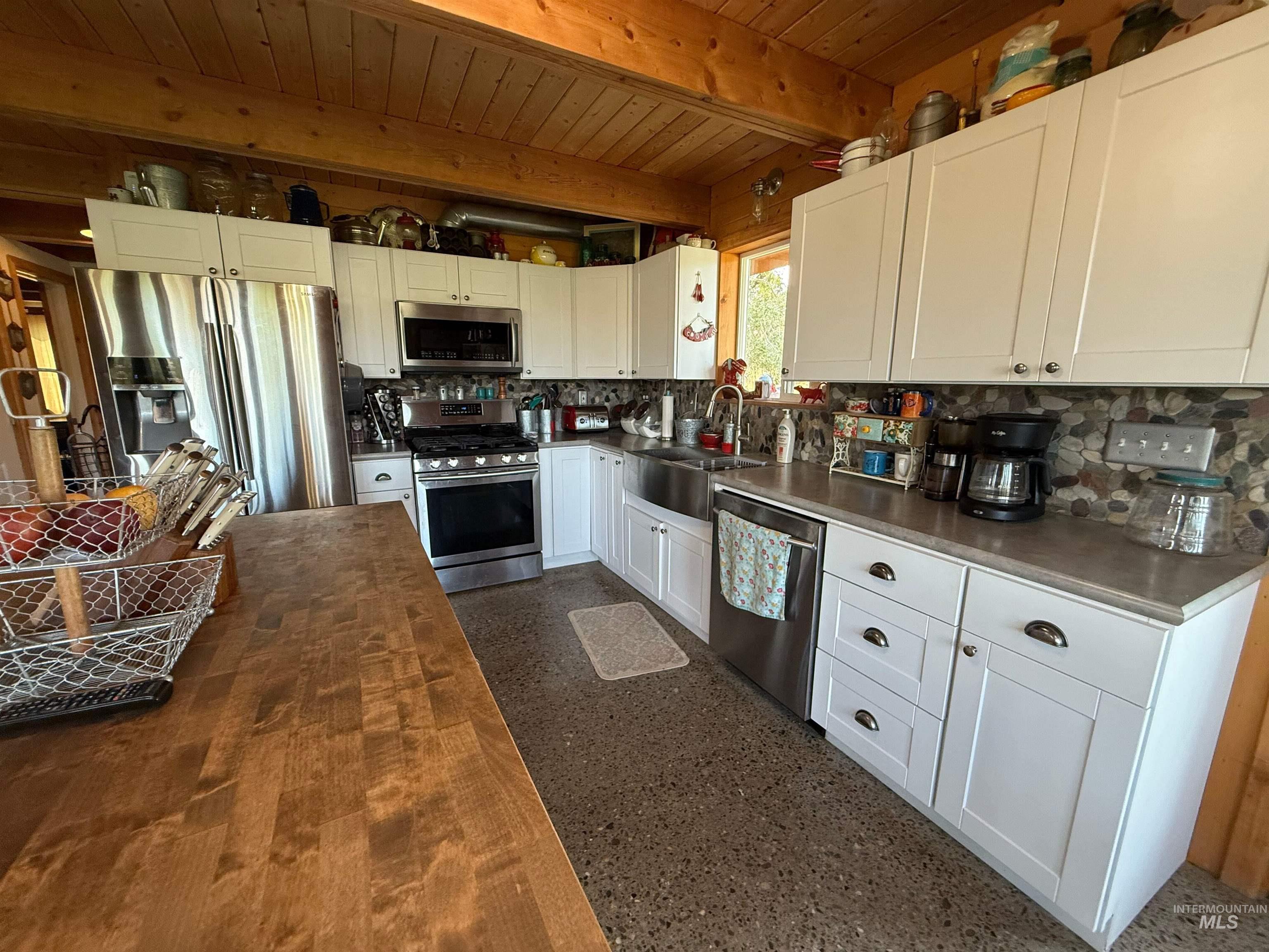 Kitchen featuring white cabinetry, appliances with stainless steel finishes, a wooden ceiling with exposed beams, light speckled floor, and tasteful backsplash