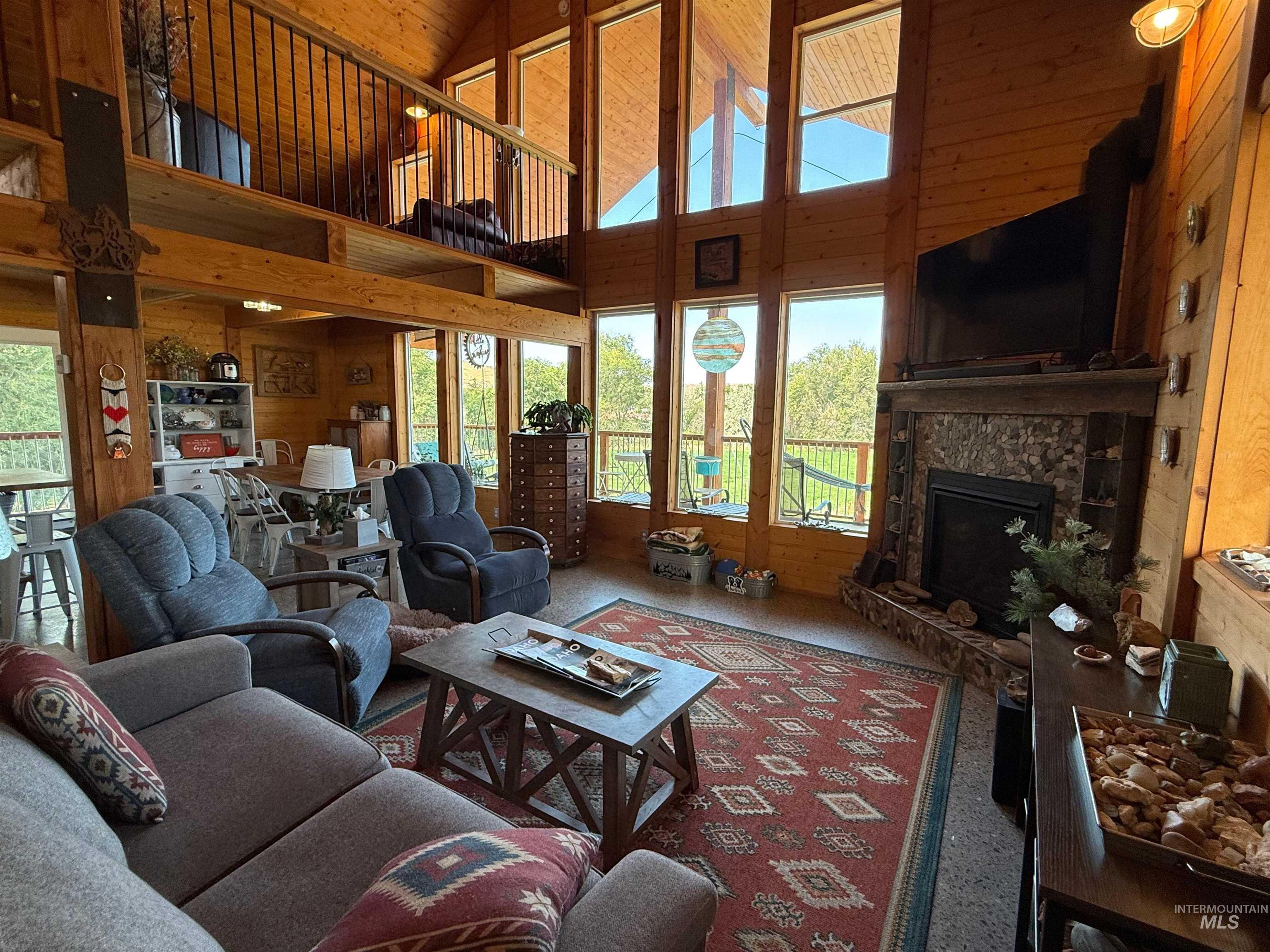 Living room with wood walls, high vaulted ceiling, a stone fireplace, and carpet floors