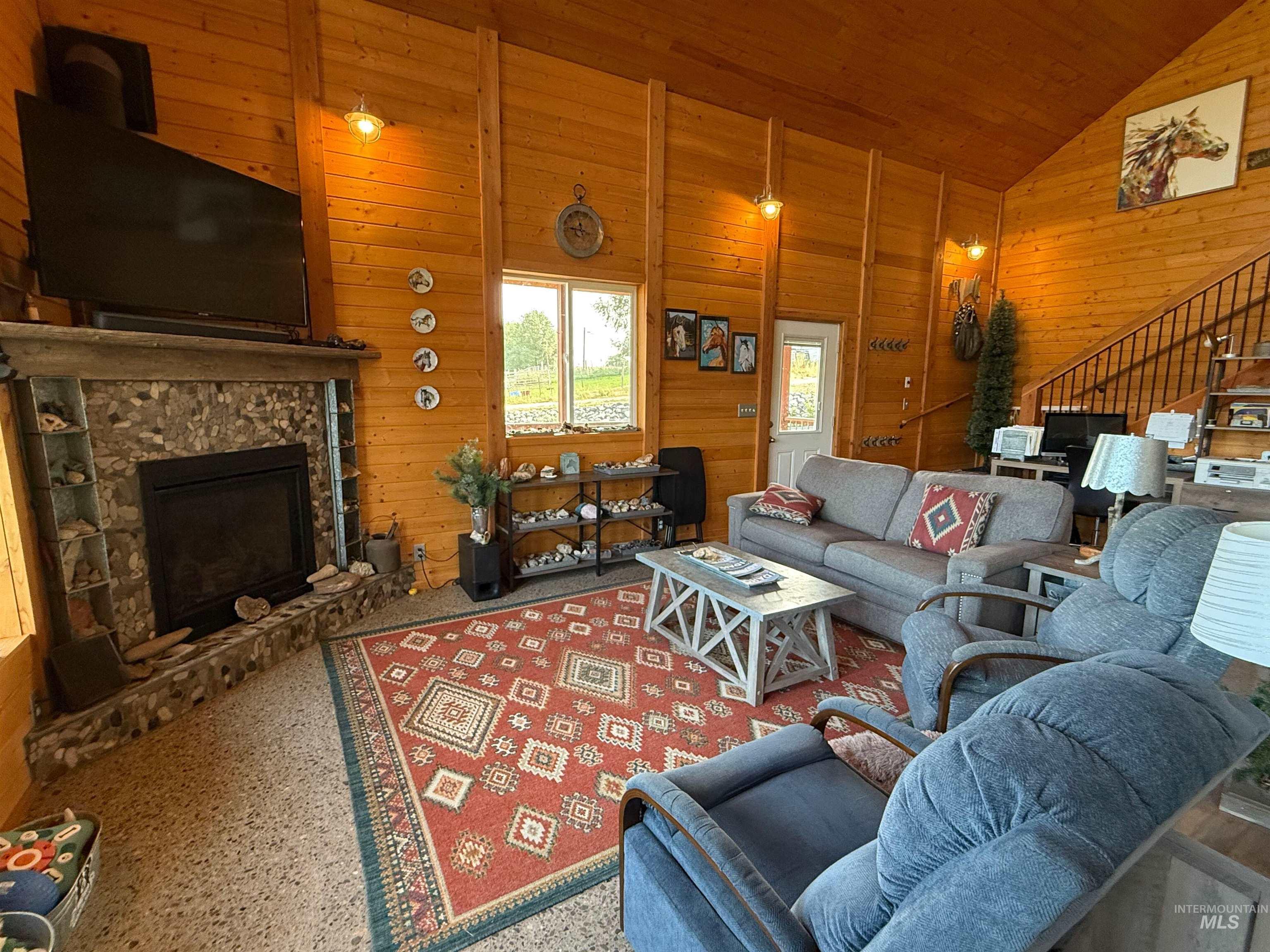 Living area with wood walls, stairs, a fireplace, high vaulted ceiling, and wood ceiling