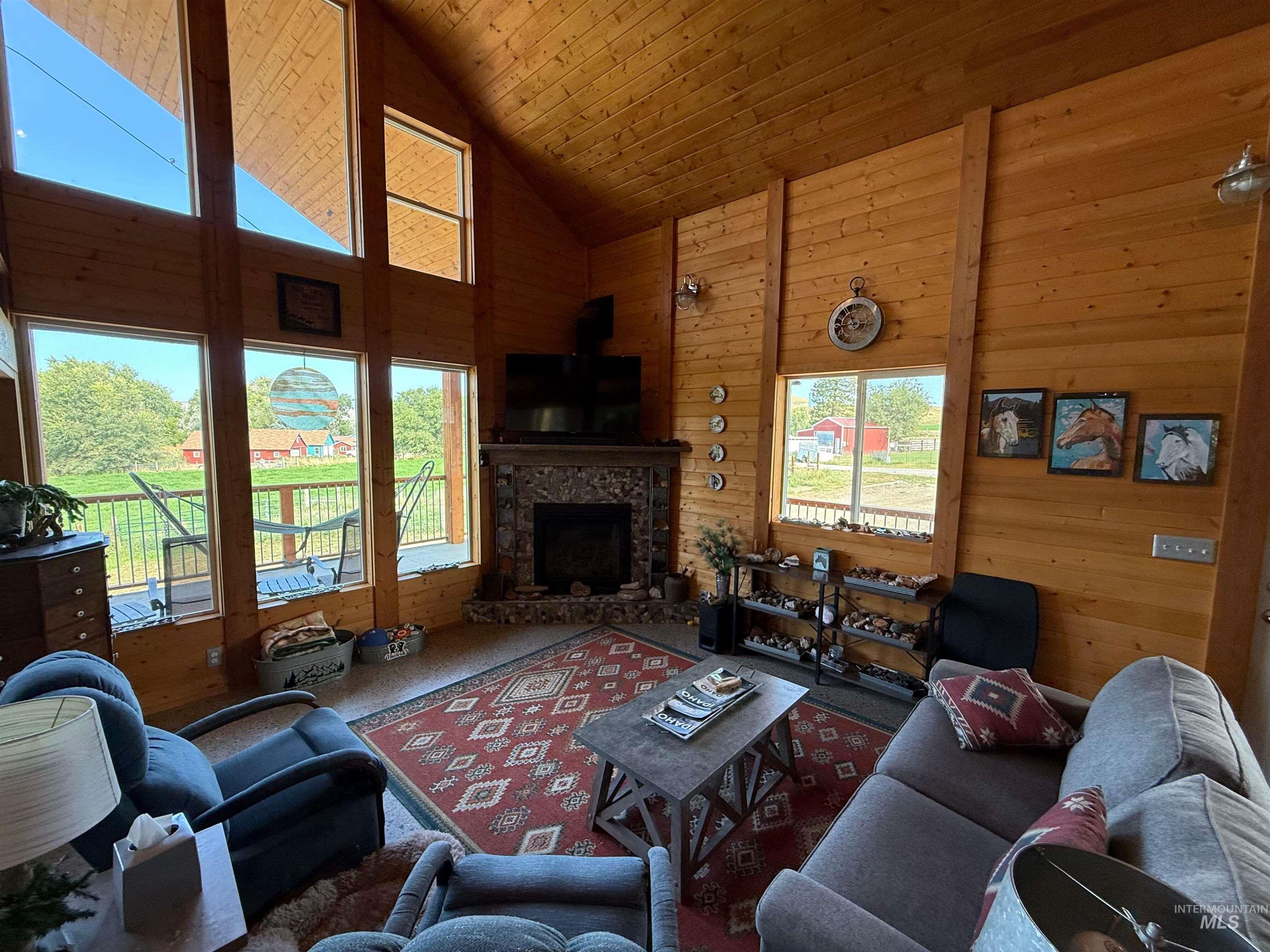 Living area featuring wooden walls, high vaulted ceiling, a stone fireplace, wooden ceiling, and carpet flooring