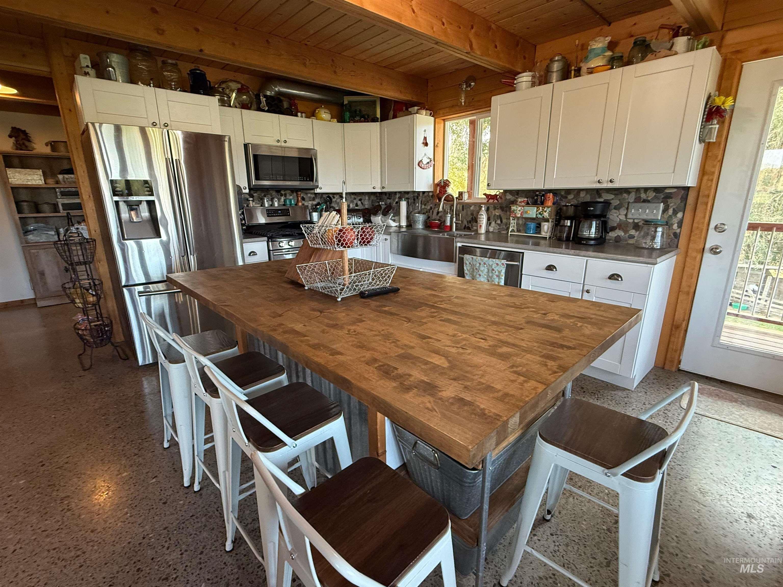 Kitchen featuring a kitchen bar, white cabinetry, appliances with stainless steel finishes, a wooden ceiling with exposed beams, and butcher block counters