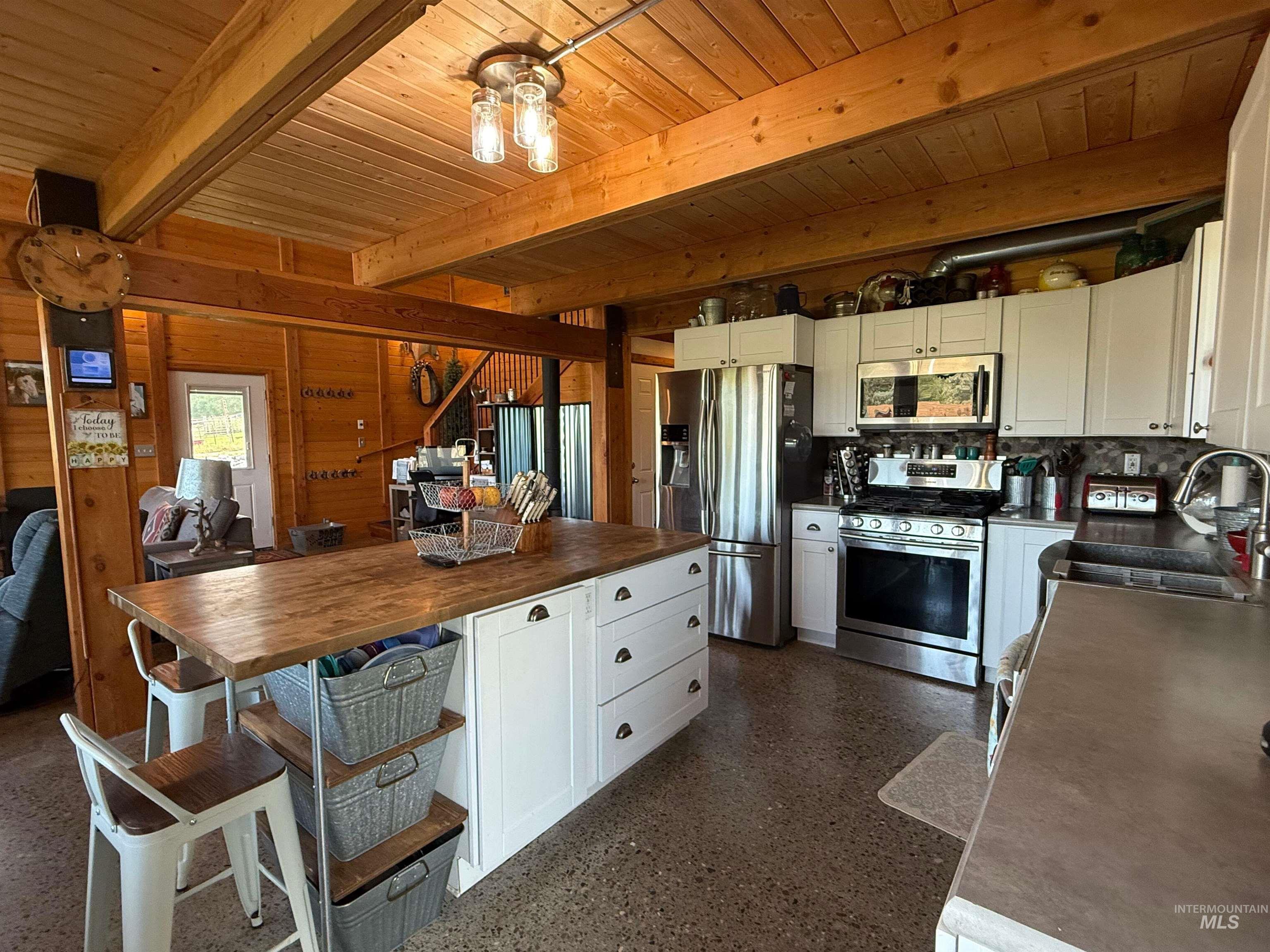 Kitchen featuring stainless steel appliances, white cabinets, a wood ceiling with exposed beams, wooden counters, and wooden walls