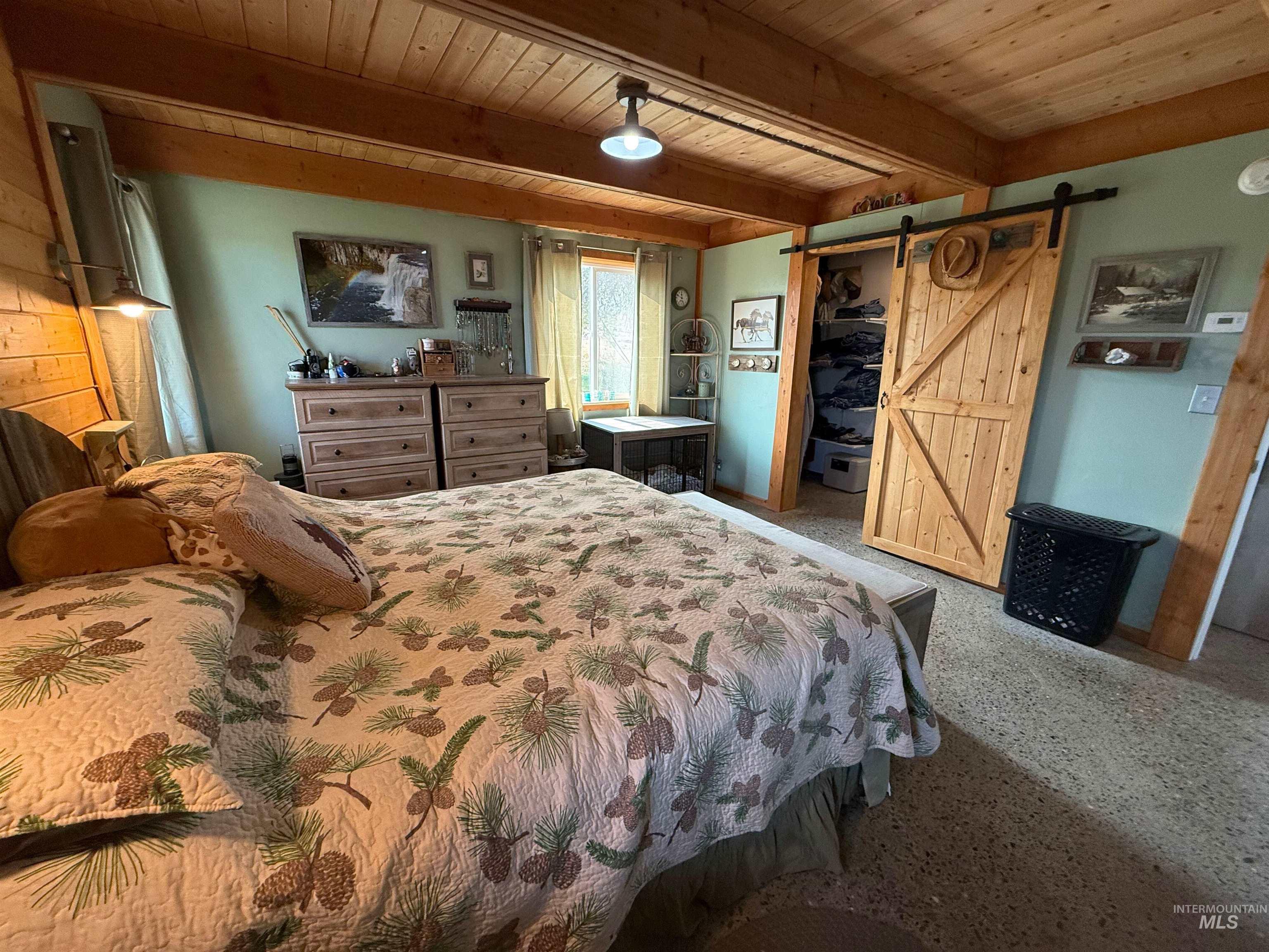Bedroom with a barn door, a wood ceiling with exposed beams, speckled floor, and a walk in closet