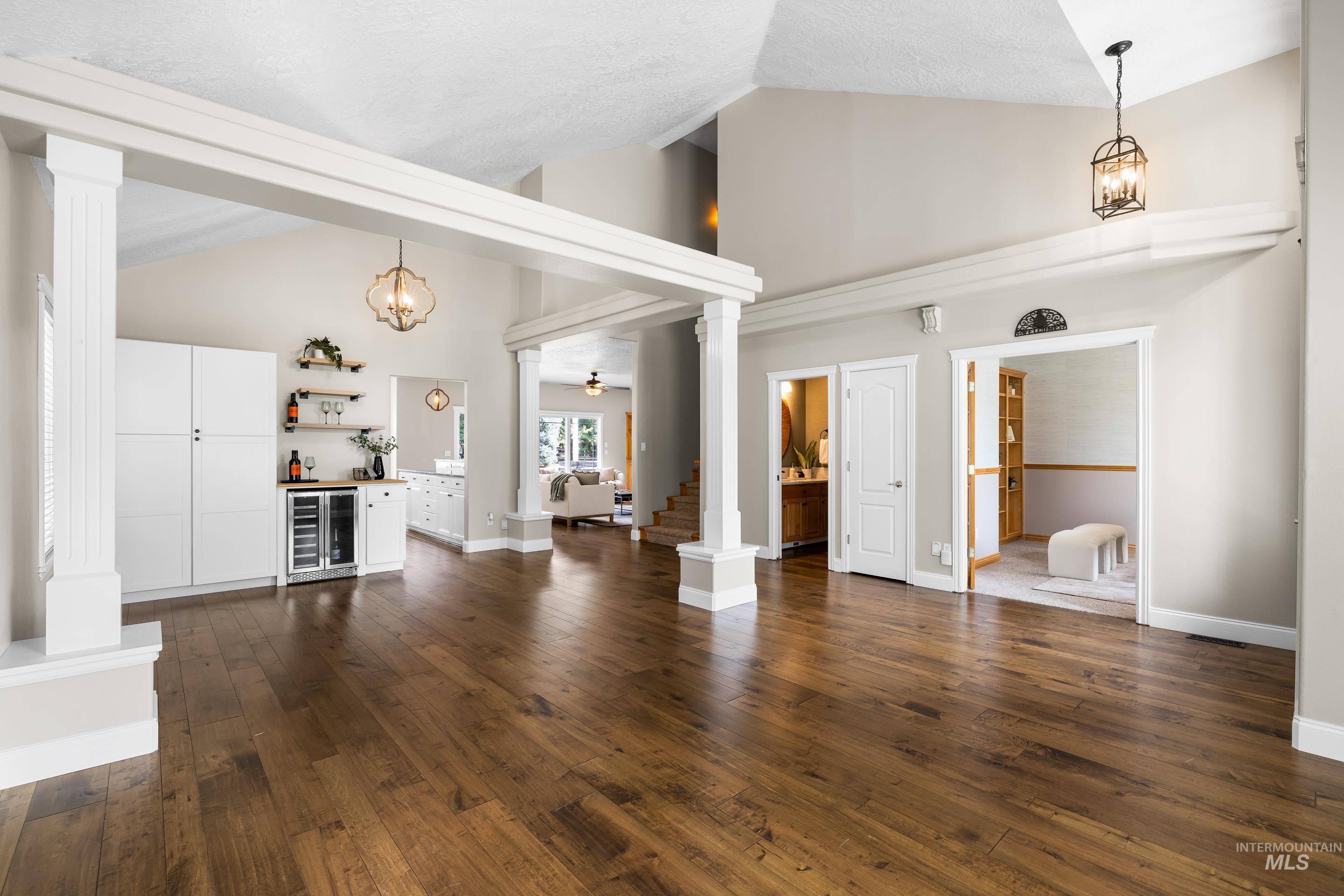 Unfurnished living room featuring high vaulted ceiling, decorative columns, a bar, a chandelier, and dark wood-style flooring