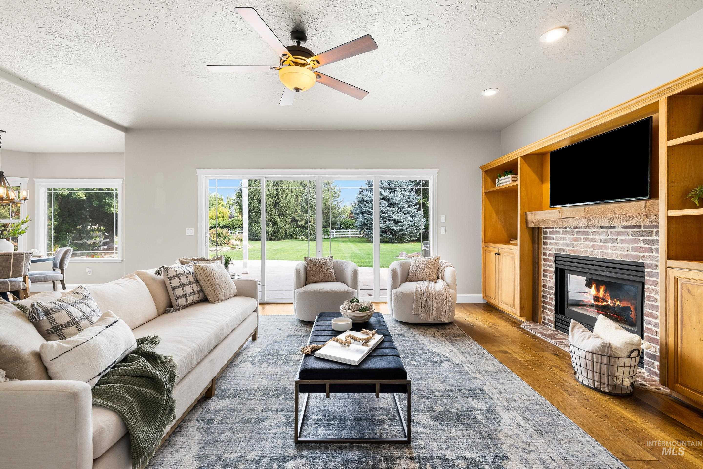 Living room with a textured ceiling, light wood finished floors, ceiling fan, a fireplace, and a chandelier