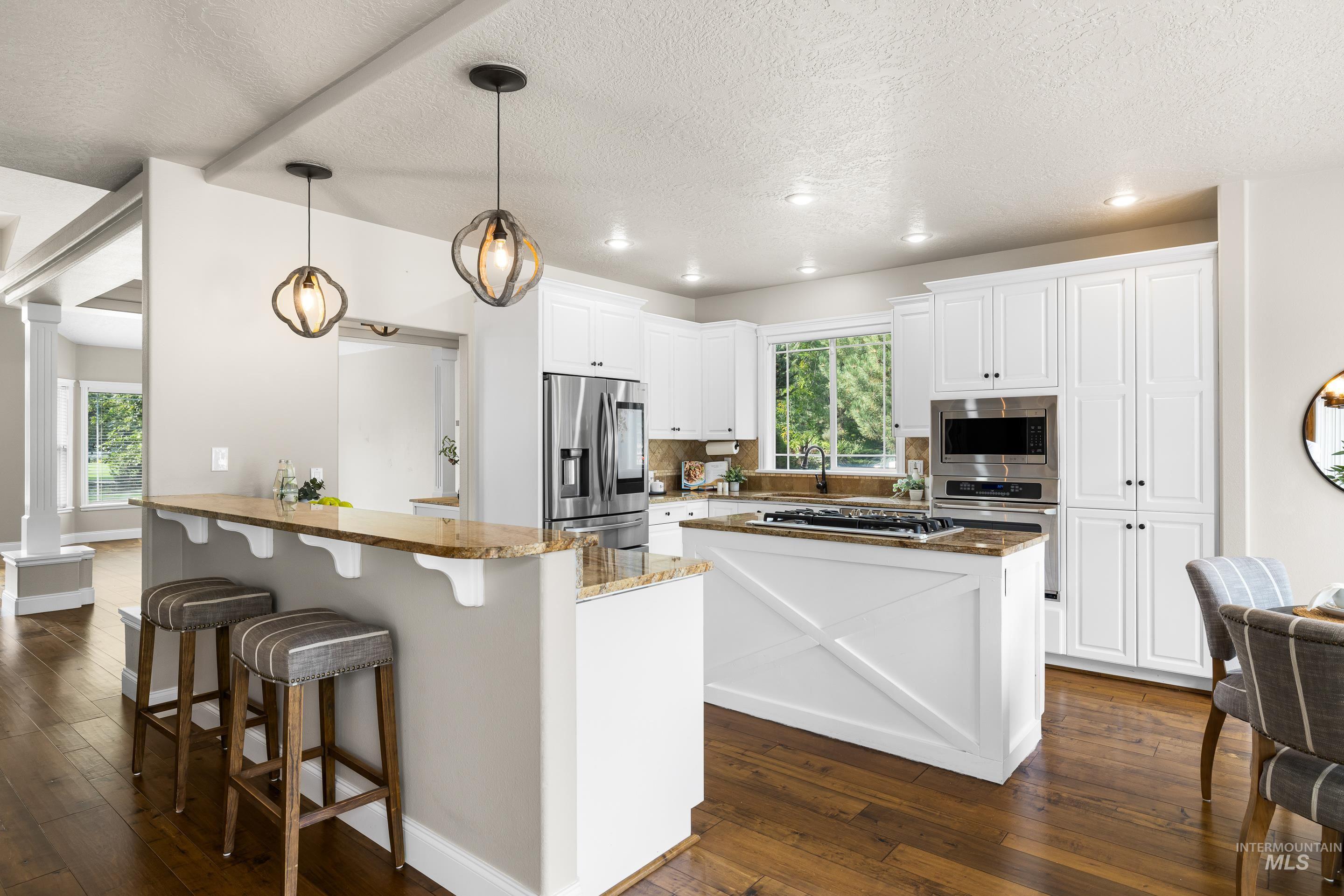 Kitchen with a peninsula, a kitchen breakfast bar, pendant lighting, white cabinets, and dark wood-type flooring