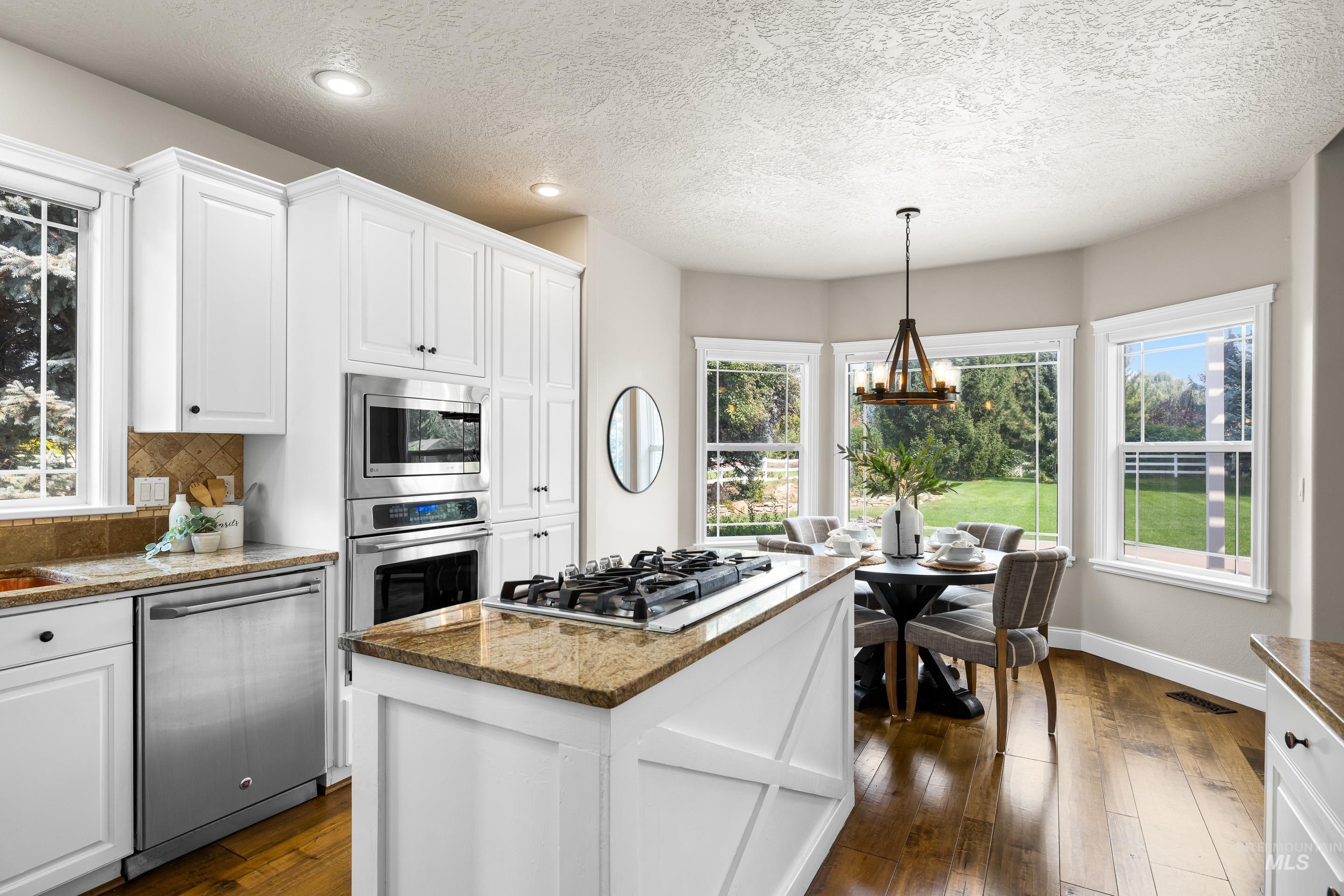 Kitchen featuring healthy amount of natural light, white cabinetry, appliances with stainless steel finishes, a kitchen island, and a textured ceiling