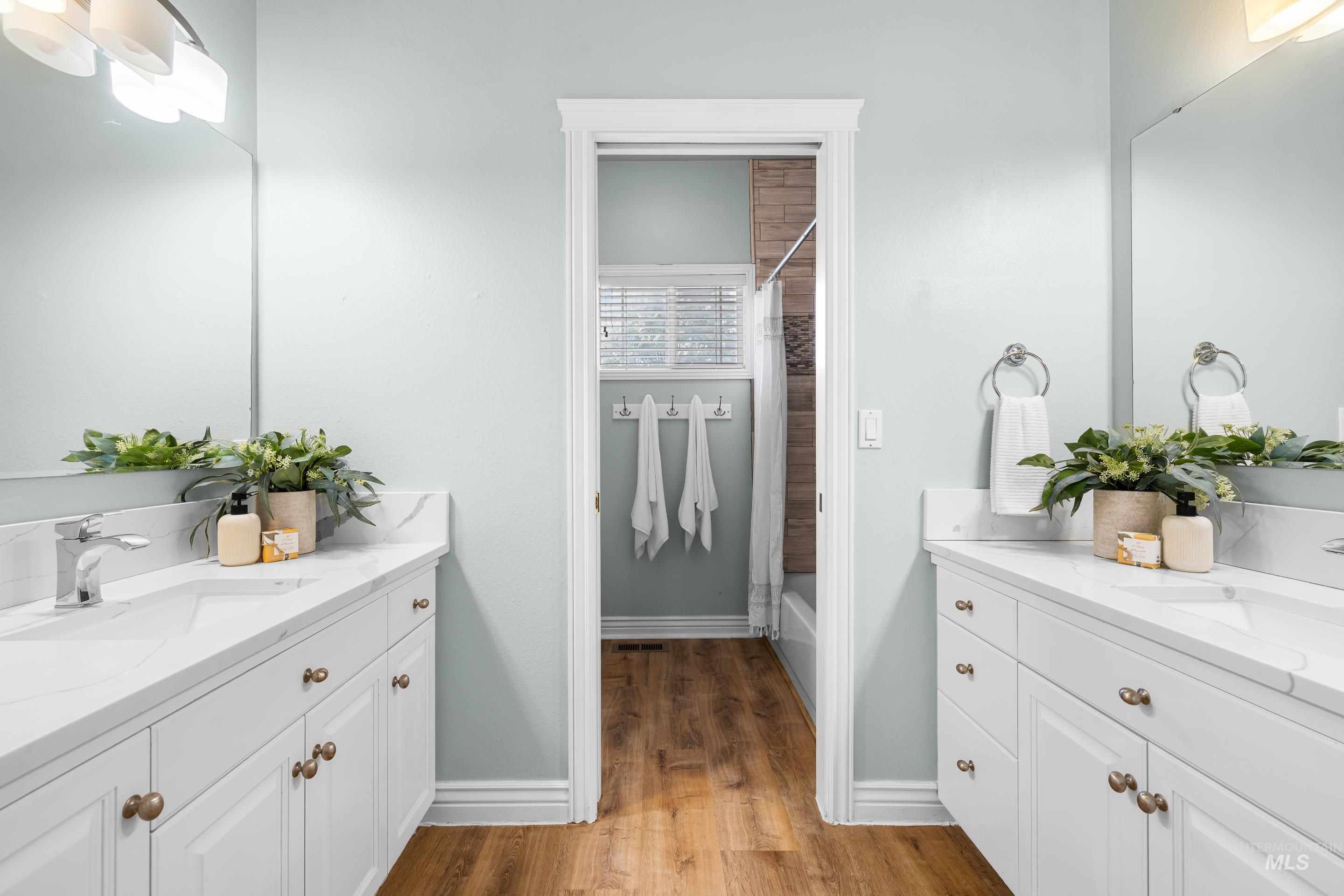 Full bathroom featuring two vanities, shower / bath combo with shower curtain, and light wood-type flooring