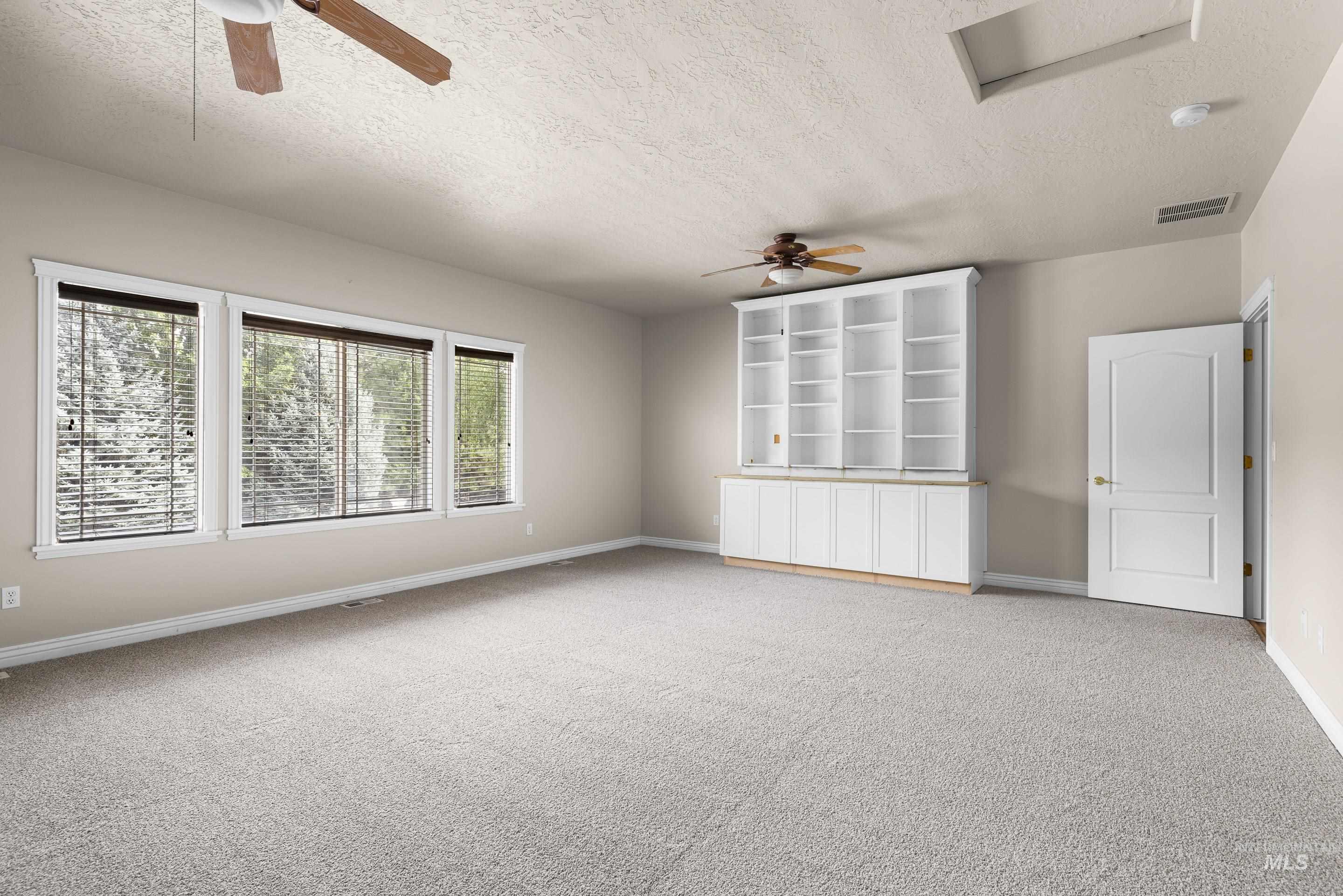 Empty room featuring a ceiling fan, a textured ceiling, and light colored carpet