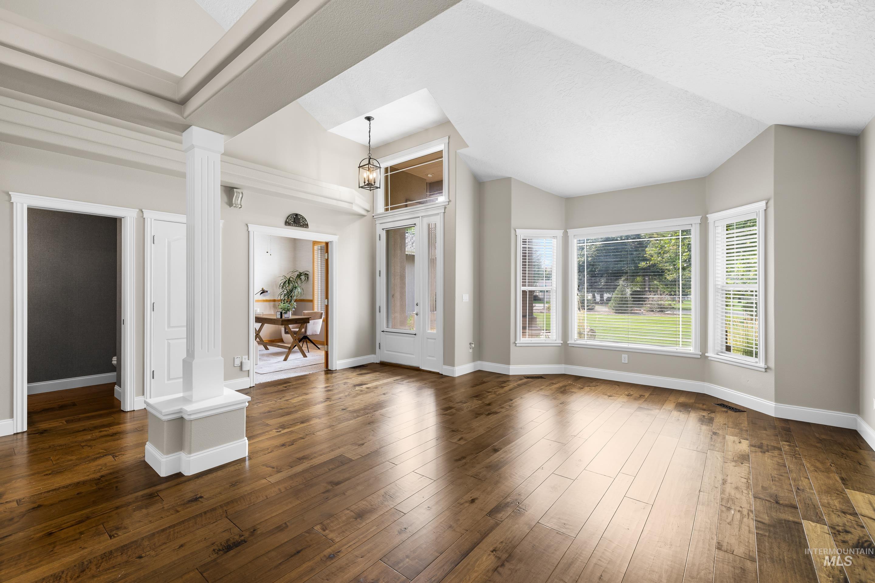 Unfurnished living room featuring dark wood-style floors, ornate columns, and a textured ceiling