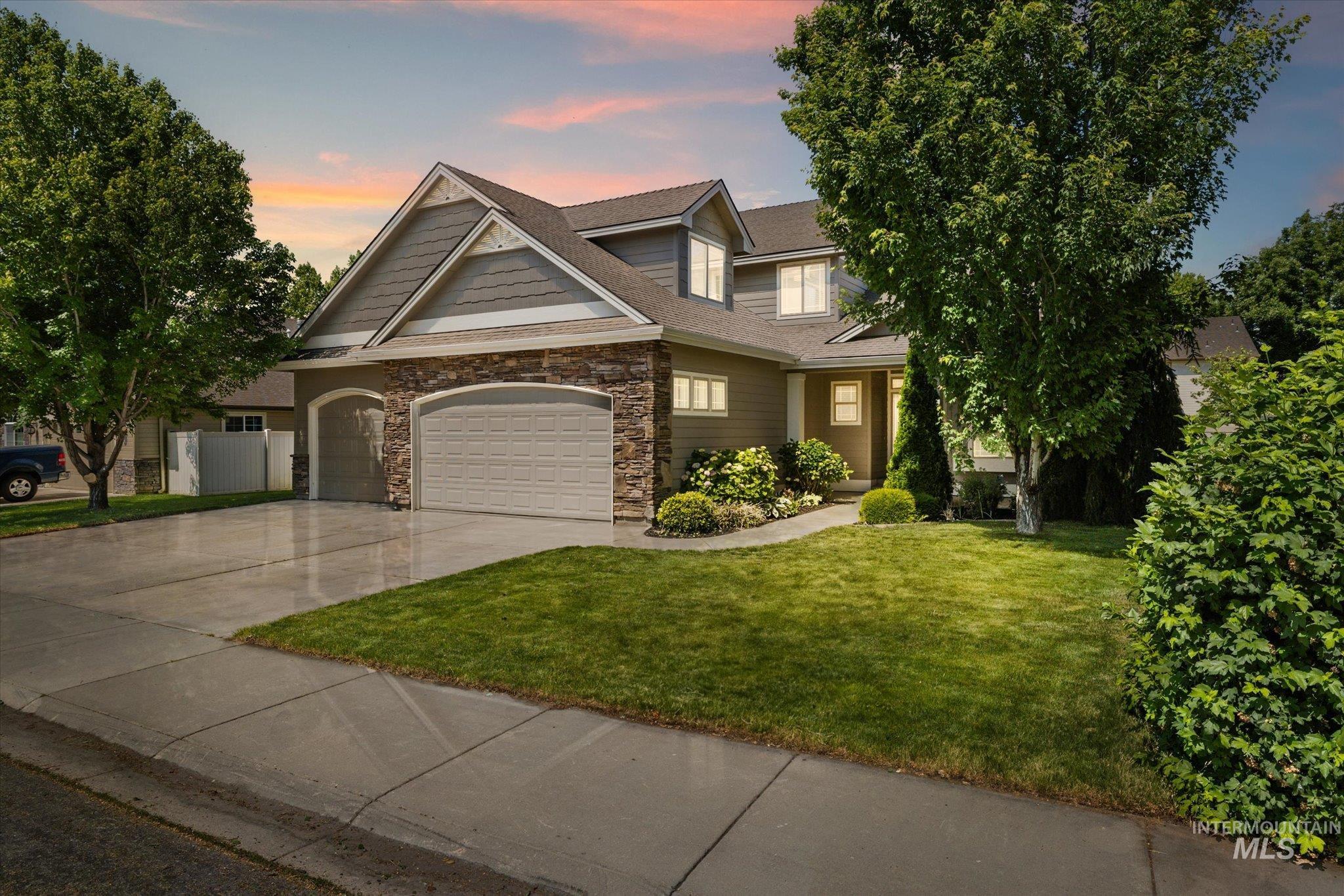 View of front facade featuring a lawn, concrete driveway, stone siding, an attached garage, and a shingled roof