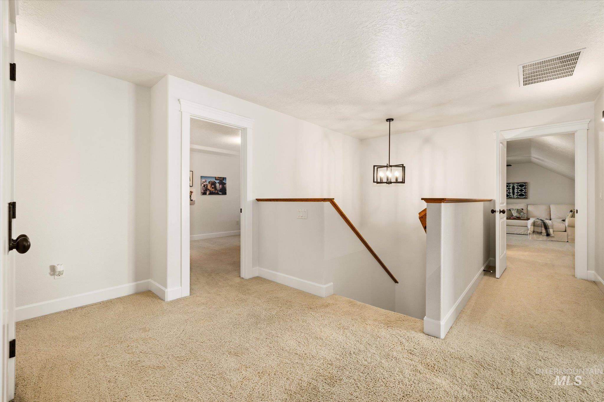Hall featuring an upstairs landing, light carpet, a textured ceiling, and a chandelier