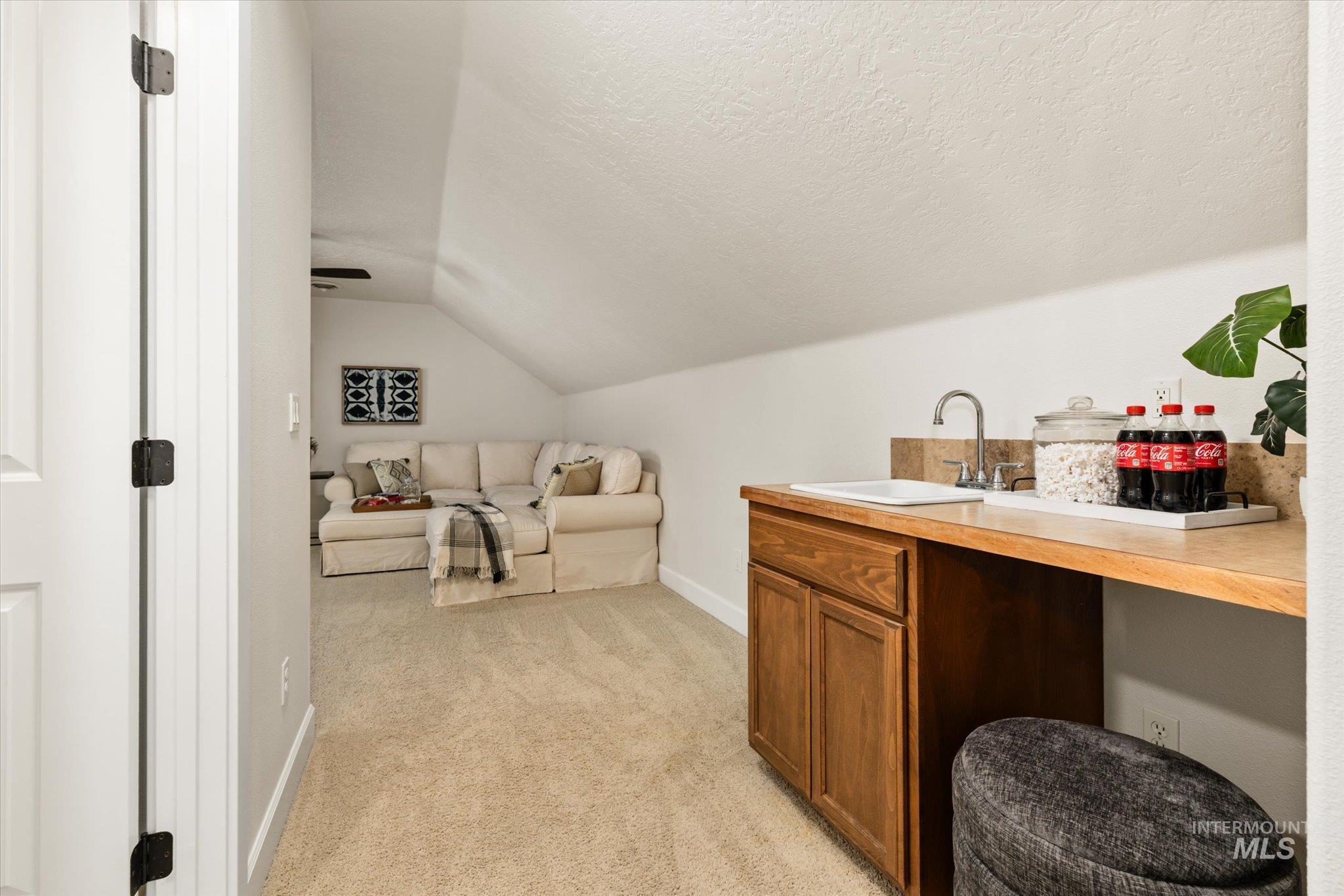 Bonus Room bar featuring vaulted ceiling, light carpet, brown cabinetry, and a textured ceiling