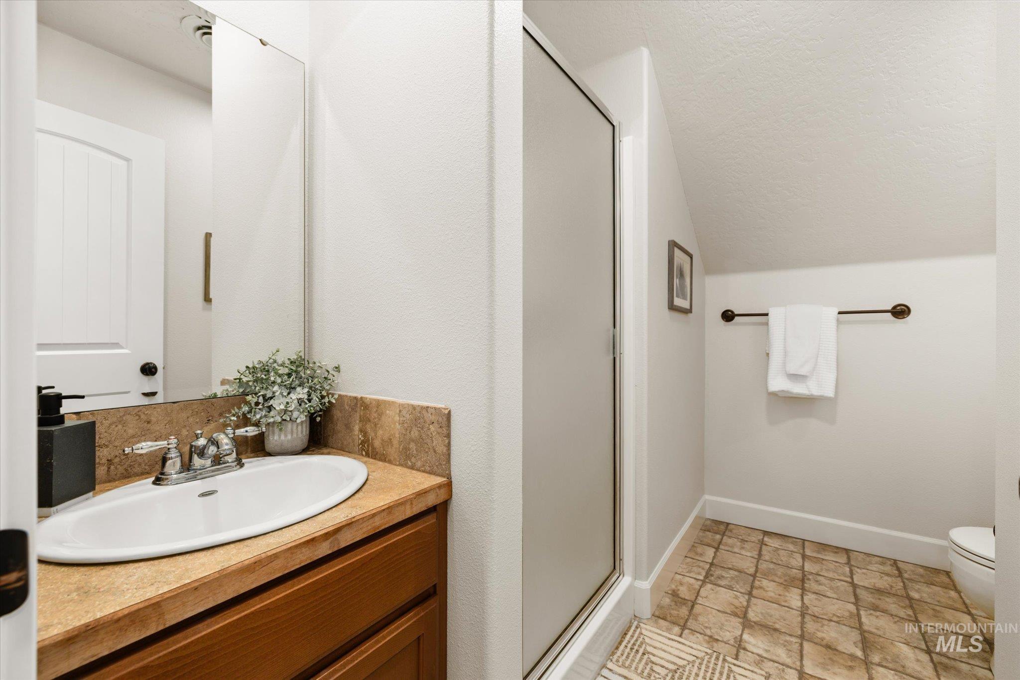 Full bathroom featuring a shower stall, vanity, vaulted ceiling, and a textured ceiling