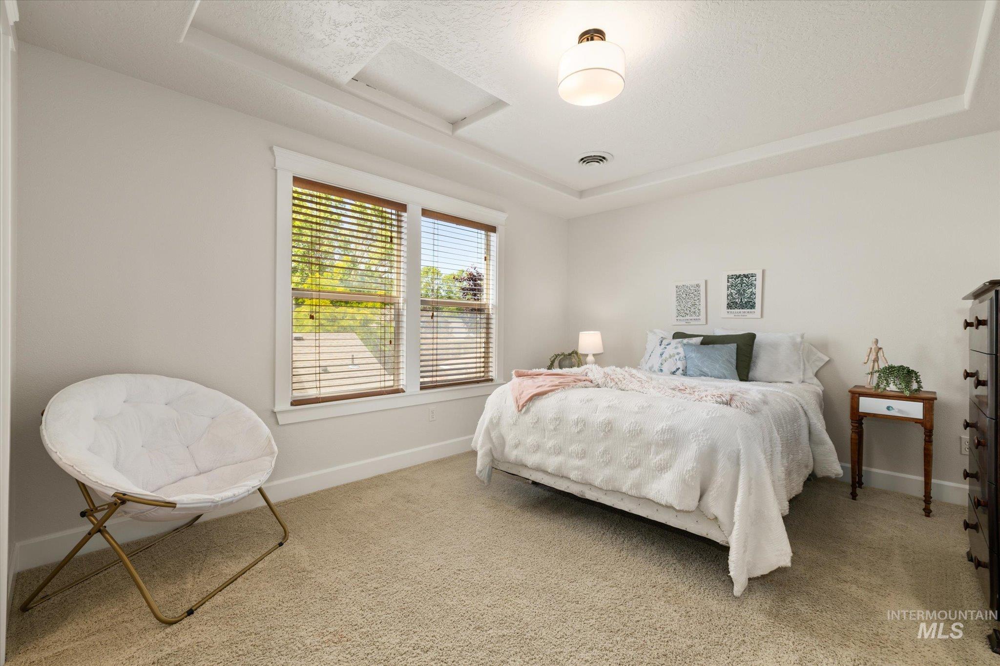 Bedroom with a raised ceiling, light carpet, attic access, and a textured ceiling