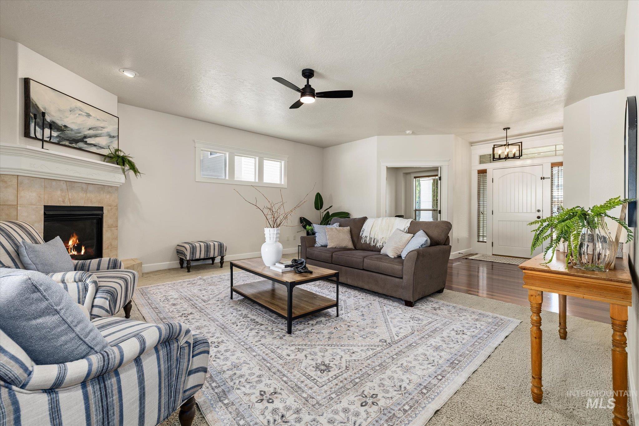 Living room with plenty of natural light, a ceiling fan, a tiled fireplace, a textured ceiling, and wood finished floors