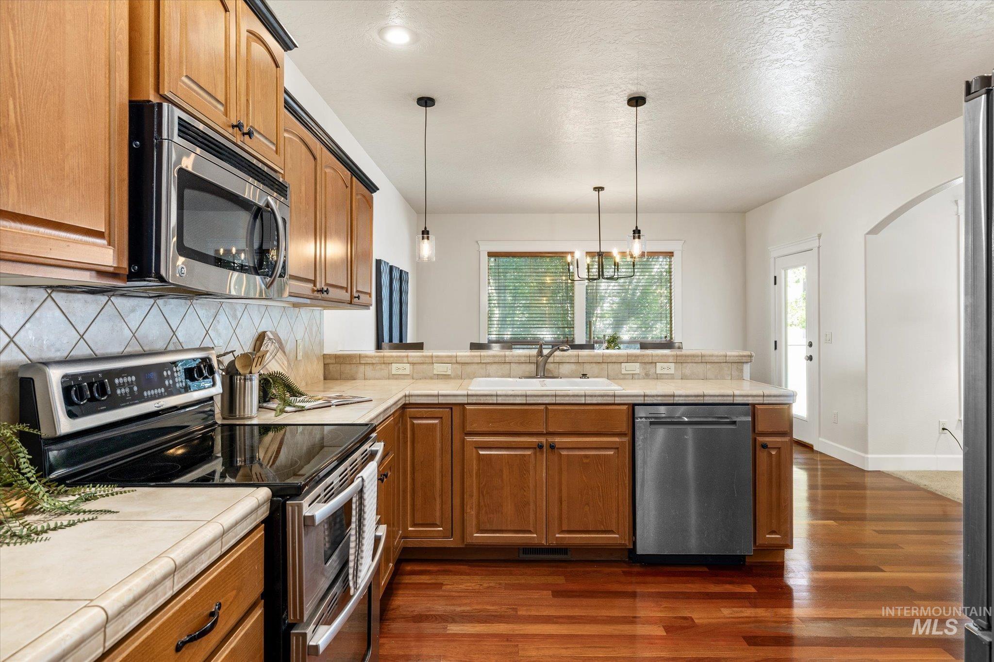 Kitchen featuring stainless steel appliances, brown cabinets, decorative backsplash, a peninsula, and a textured ceiling