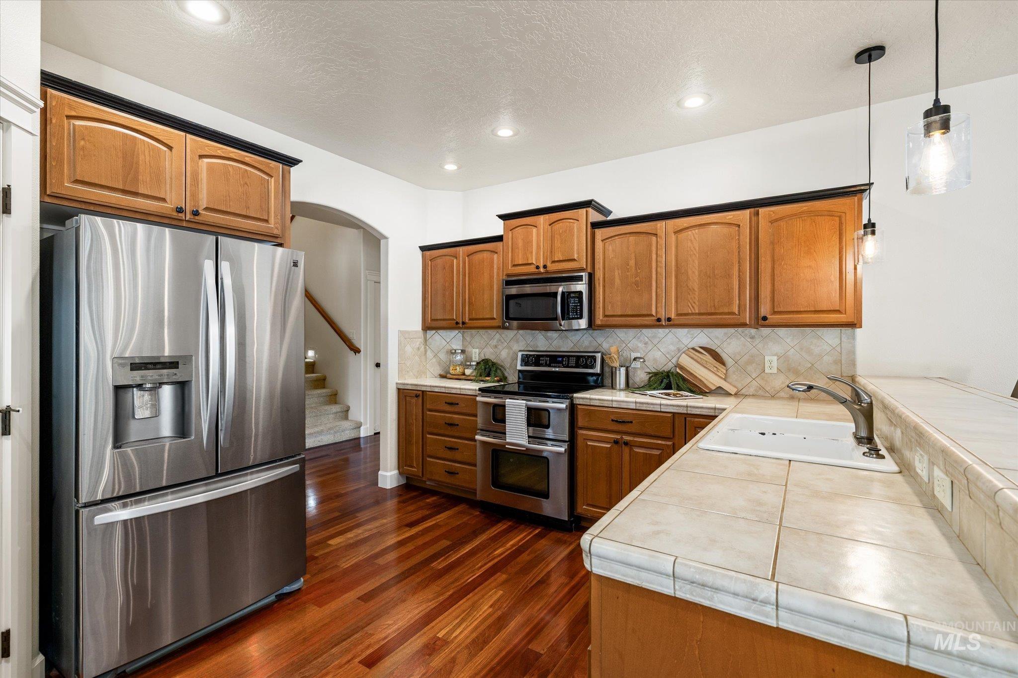 Kitchen featuring appliances with stainless steel finishes, brown cabinetry, arched walkways, tasteful backsplash, and a textured ceiling