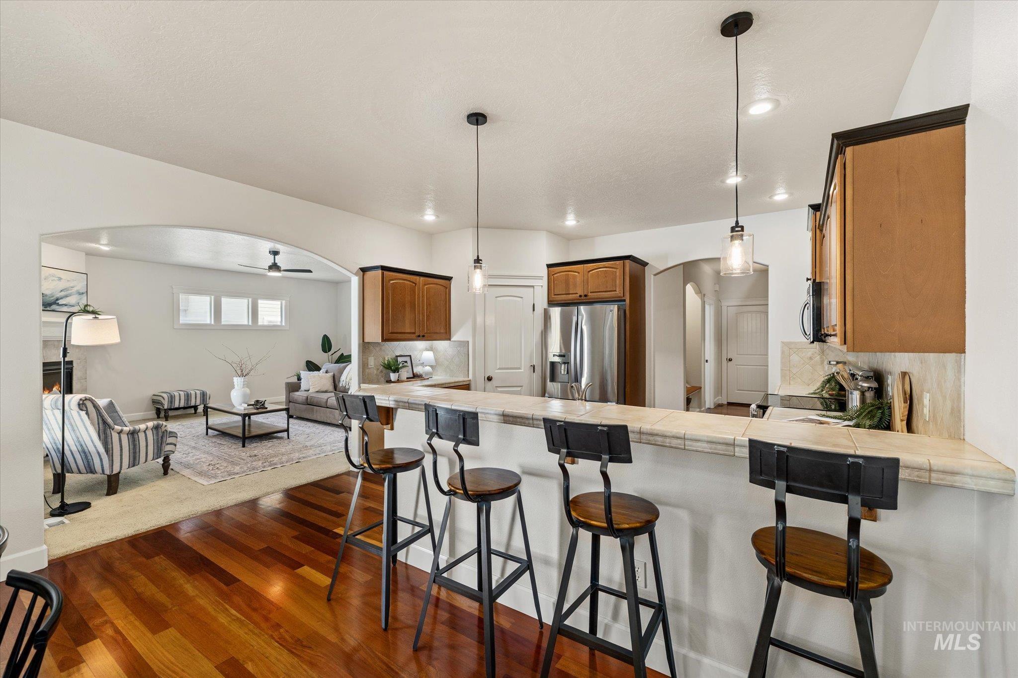 Kitchen featuring arched walkways, tile counters, a breakfast bar, dark wood-style floors, and stainless steel appliances