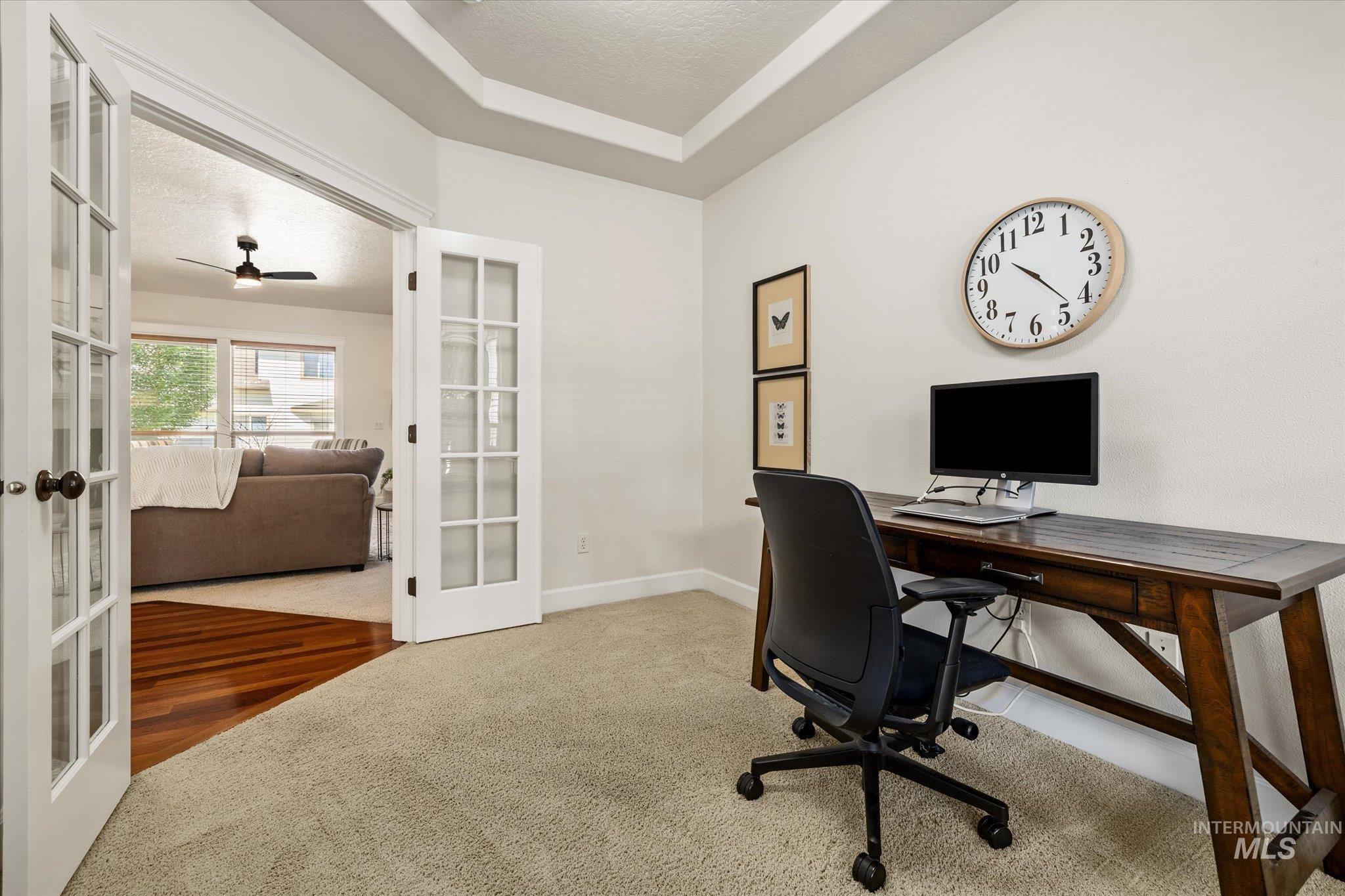 Office space with french doors, carpet floors, a textured ceiling, a raised ceiling, and a ceiling fan