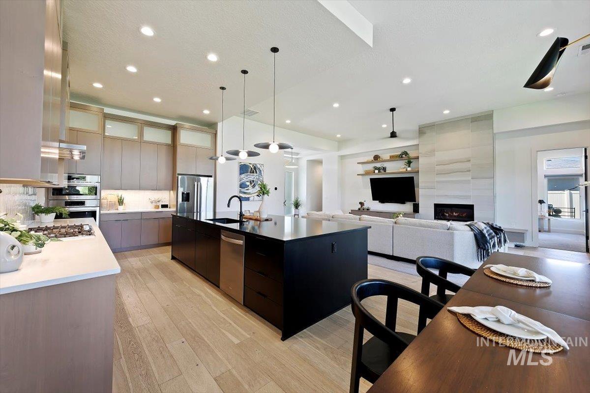 Kitchen featuring modern cabinets, hanging light fixtures, an island with sink, light wood-type flooring, and open floor plan
