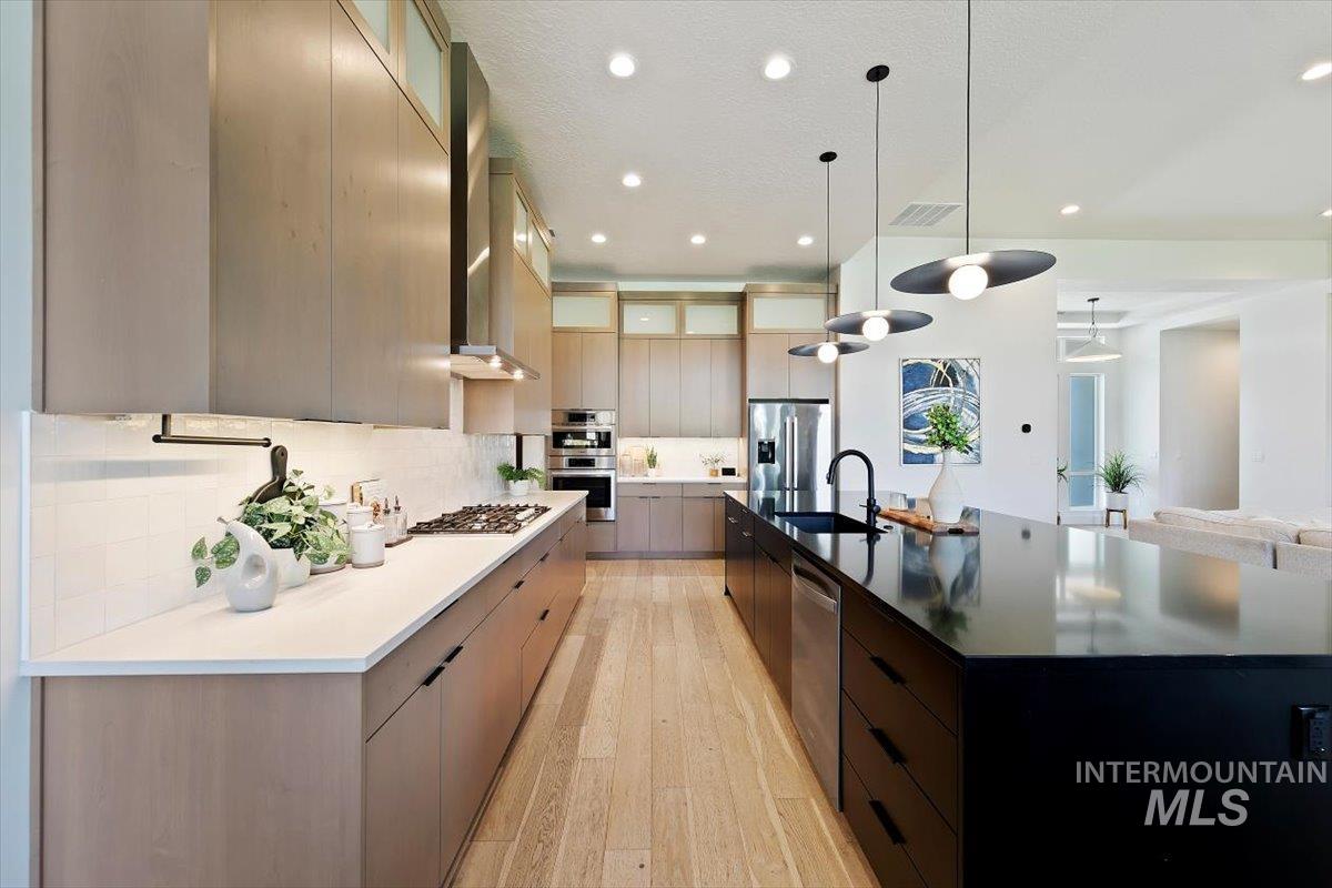 Kitchen featuring modern cabinets, hanging light fixtures, decorative backsplash, a spacious island, and light wood-style flooring