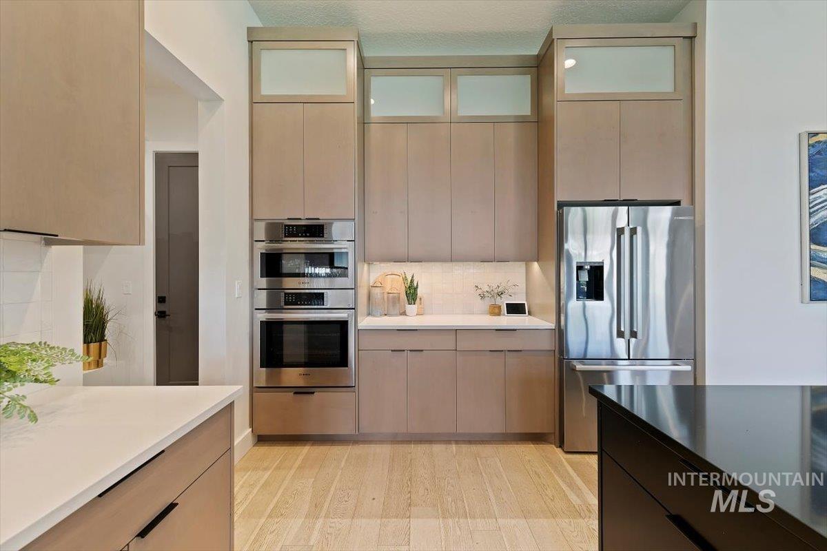 Kitchen with appliances with stainless steel finishes, light wood-type flooring, light brown cabinets, and decorative backsplash
