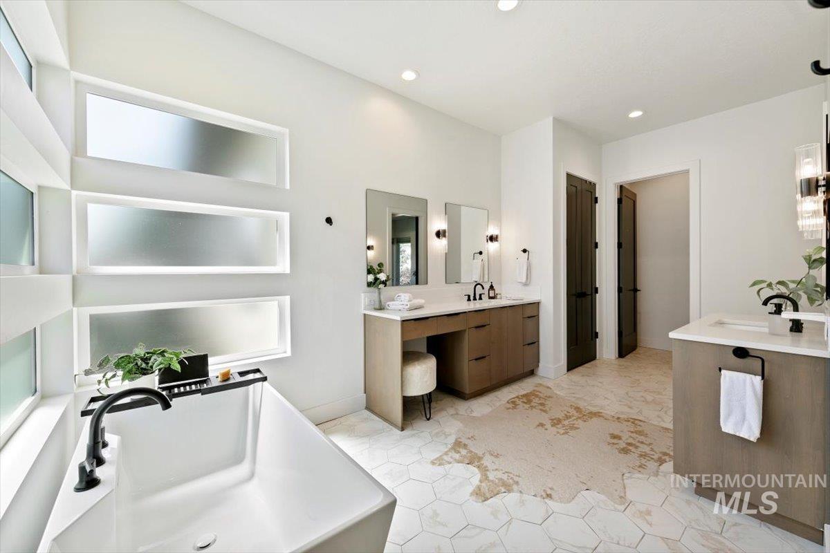 Full bathroom with two vanities, a freestanding tub, light tile patterned floors, and recessed lighting