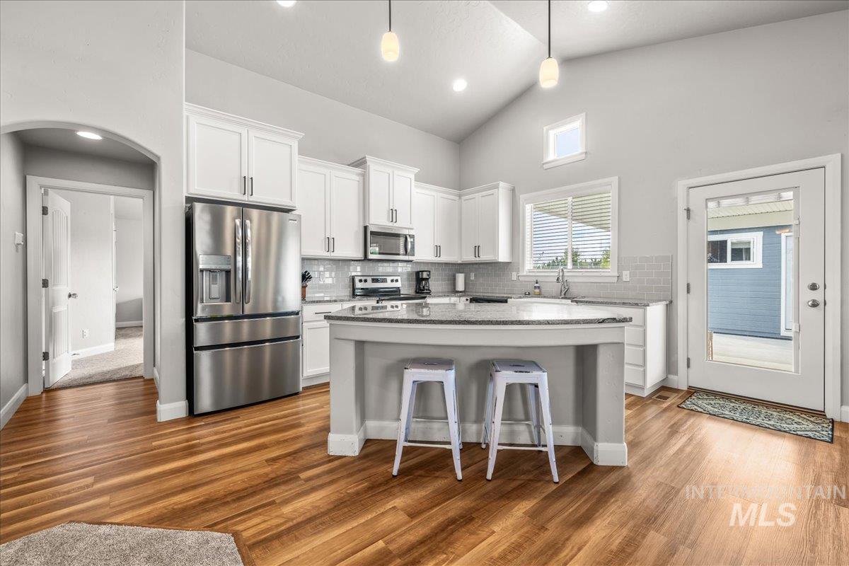 Kitchen with stainless steel appliances, backsplash, white cabinetry, a kitchen bar, and light stone counters