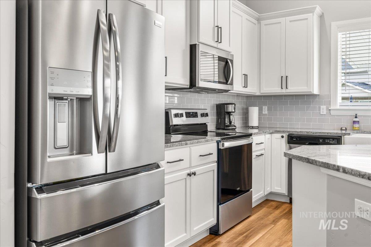Kitchen featuring stainless steel appliances, light stone counters, white cabinetry, tasteful backsplash, and light wood-style flooring