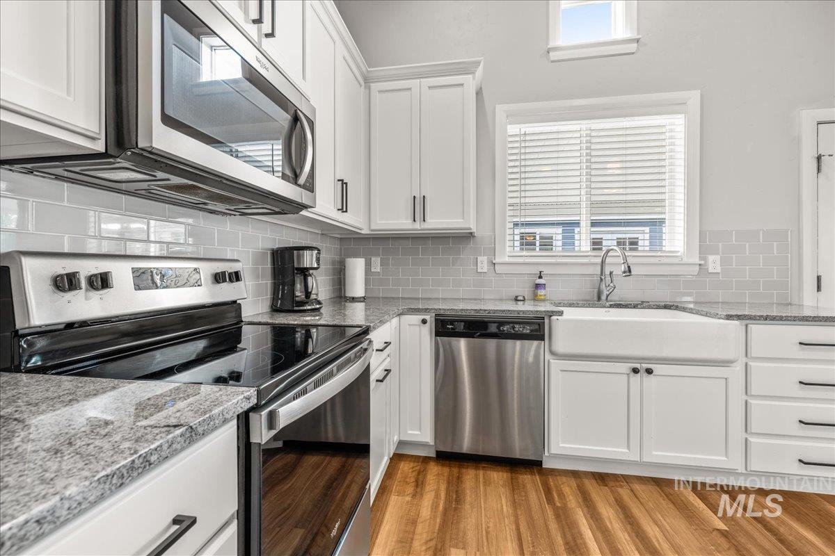 Kitchen with appliances with stainless steel finishes, white cabinets, backsplash, light wood-type flooring, and light stone counters