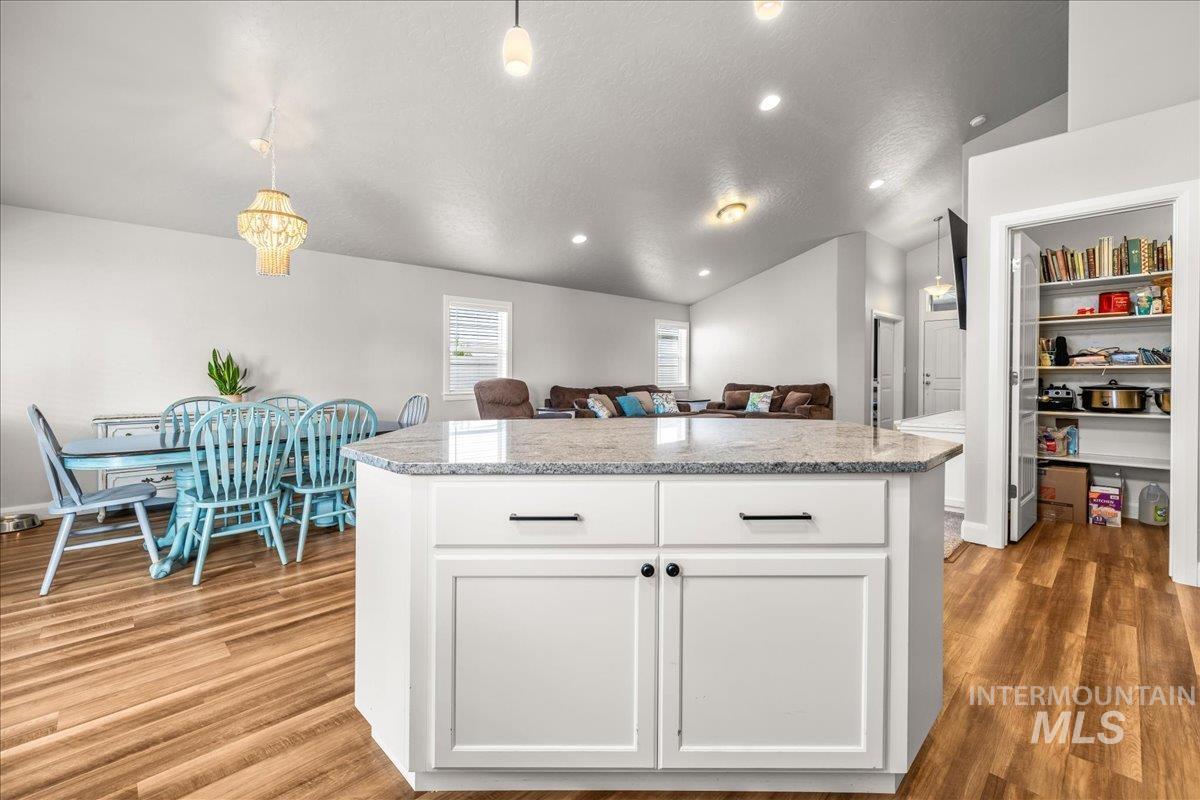 Kitchen with hanging light fixtures, vaulted ceiling, white cabinets, a kitchen island, and light wood-style floors
