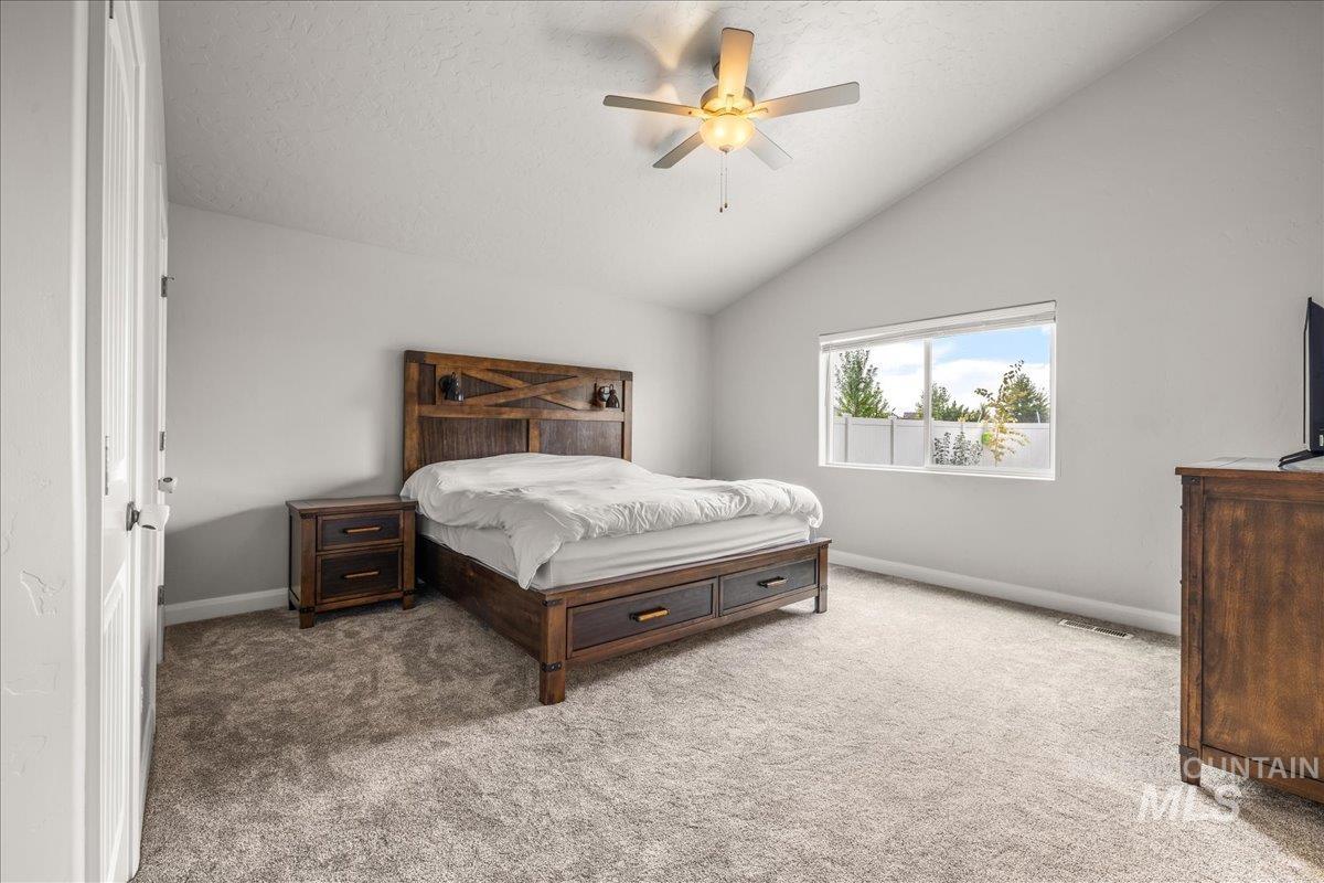 Carpeted bedroom featuring vaulted ceiling, ceiling fan, and a textured ceiling