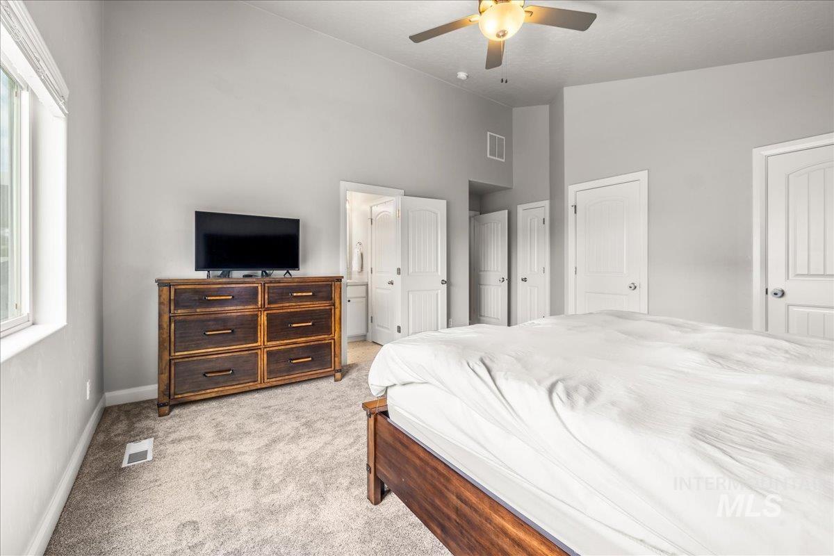 Bedroom with light carpet, ceiling fan, vaulted ceiling, and ensuite bathroom