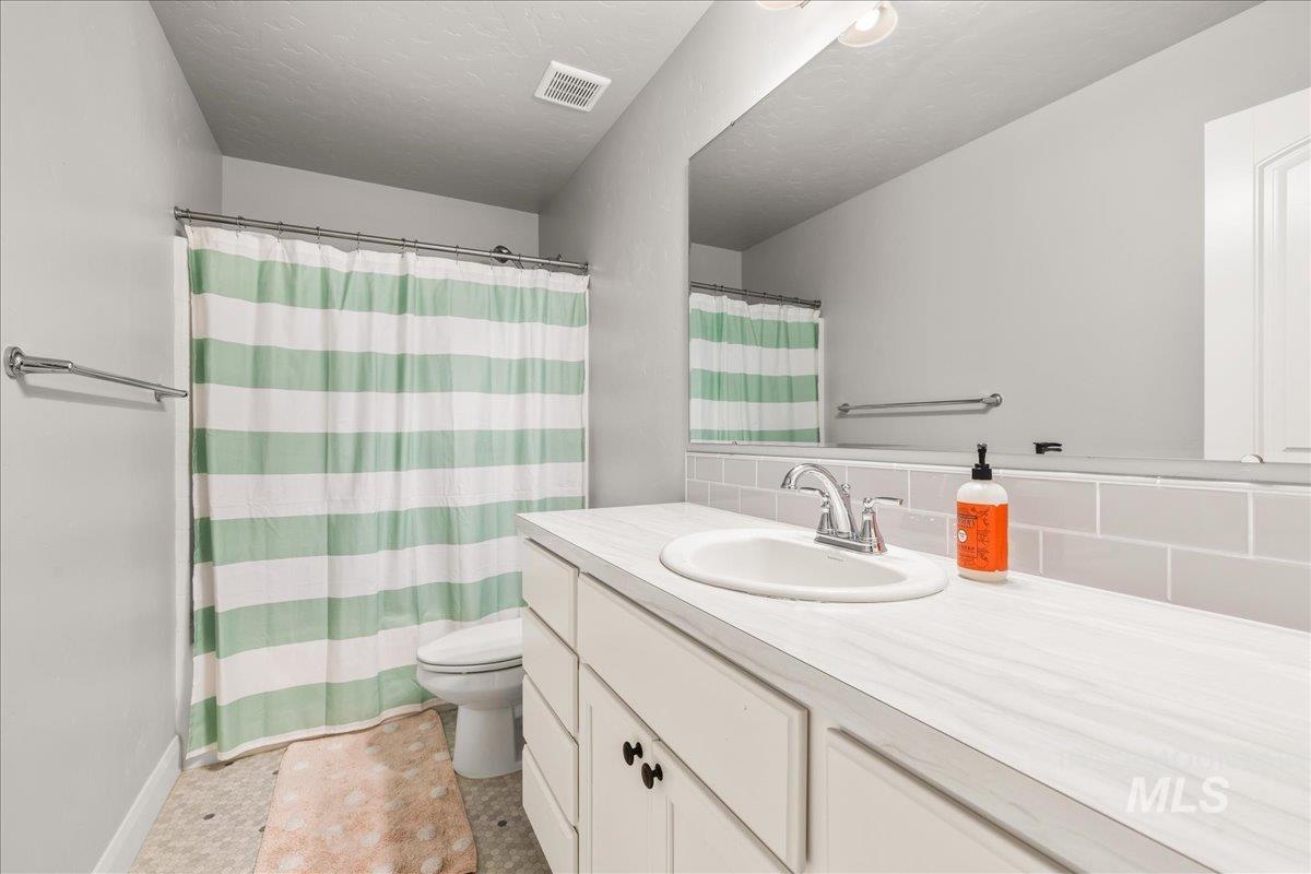 Bathroom with vanity, a textured ceiling, curtained shower, and backsplash